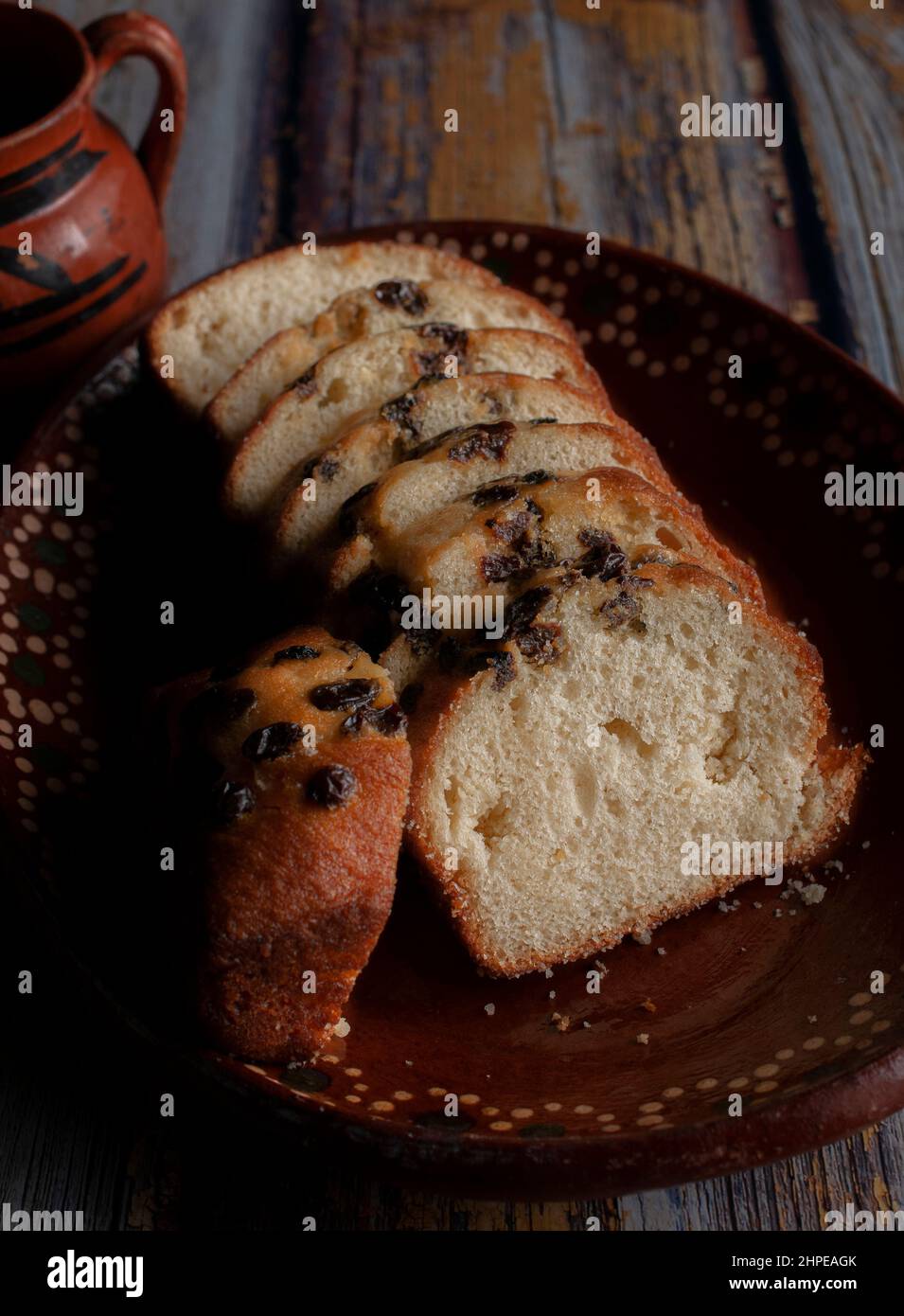 Un piatto di argilla o fango messicano fatto a mano, con pane dolce e uvetta sulla parte superiore e una tazza fumante di caffè o cioccolata calda sullo sfondo. Foto Stock