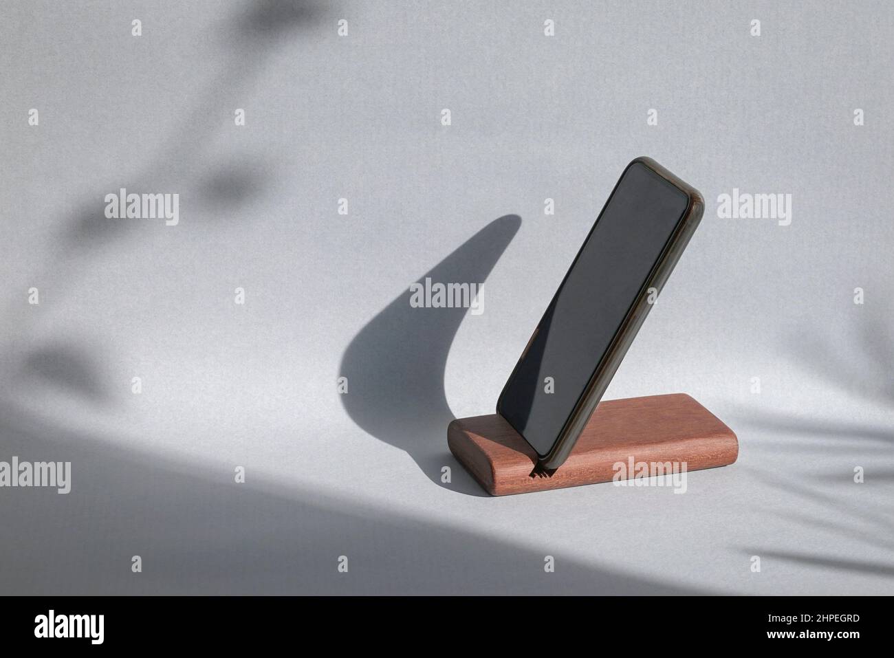 Smartphone su un supporto, mockup con ombra sullo sfondo della parete. Modello mockup per i prodotti estivi. Foto Stock