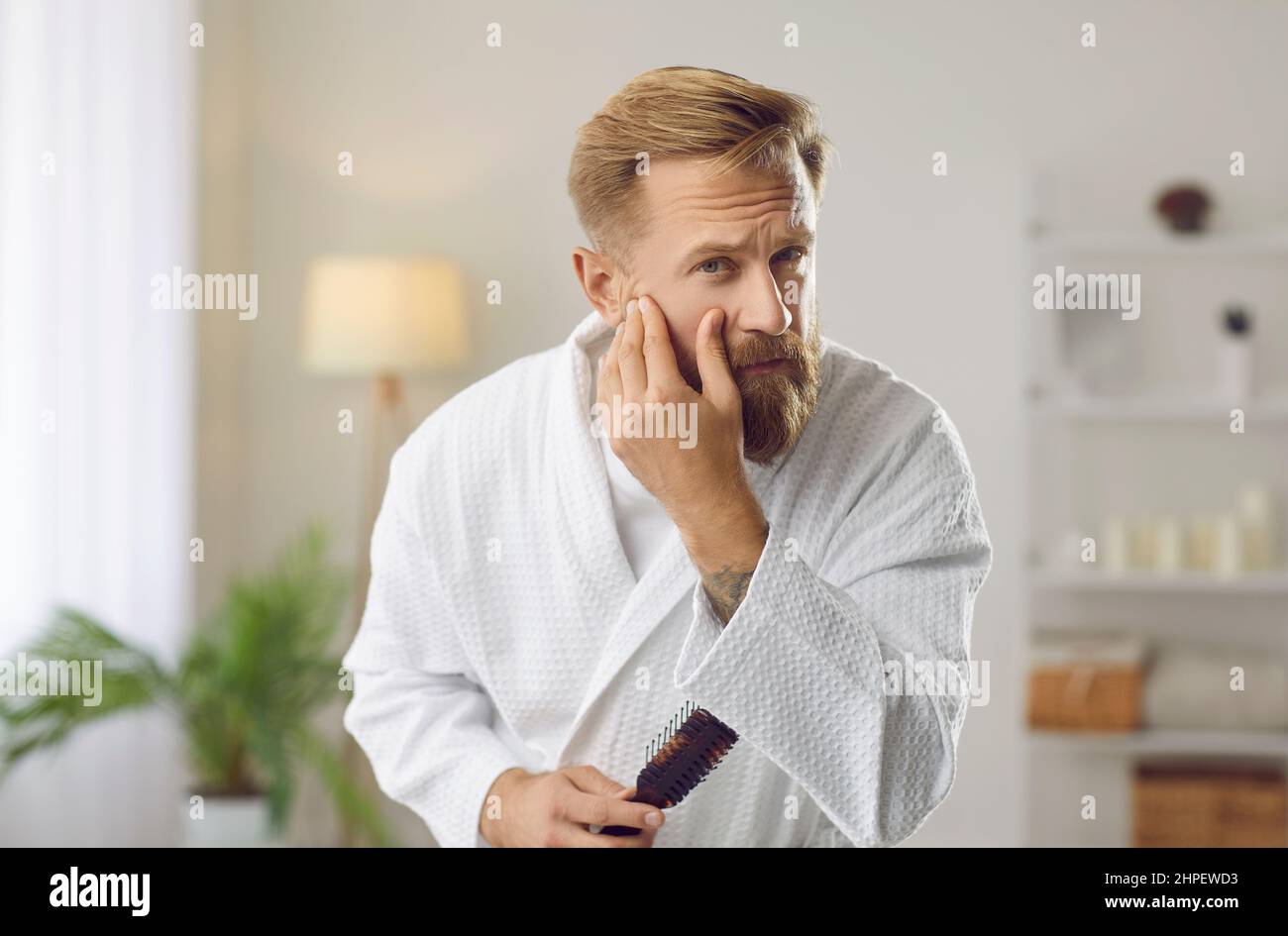 Uomo che esamina il suo volto al mattino controllando la condizione della pelle e la presenza di rughe. Foto Stock