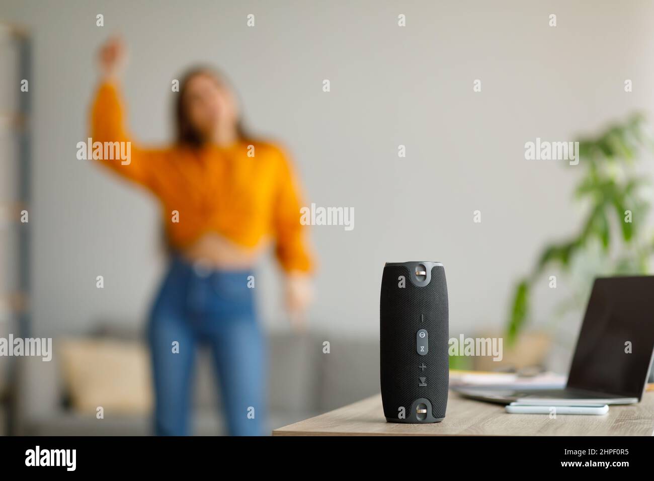Giovane donna che balla a musica popolare a casa, fuoco selettivo su speaker wireless portatile, spazio copia Foto Stock