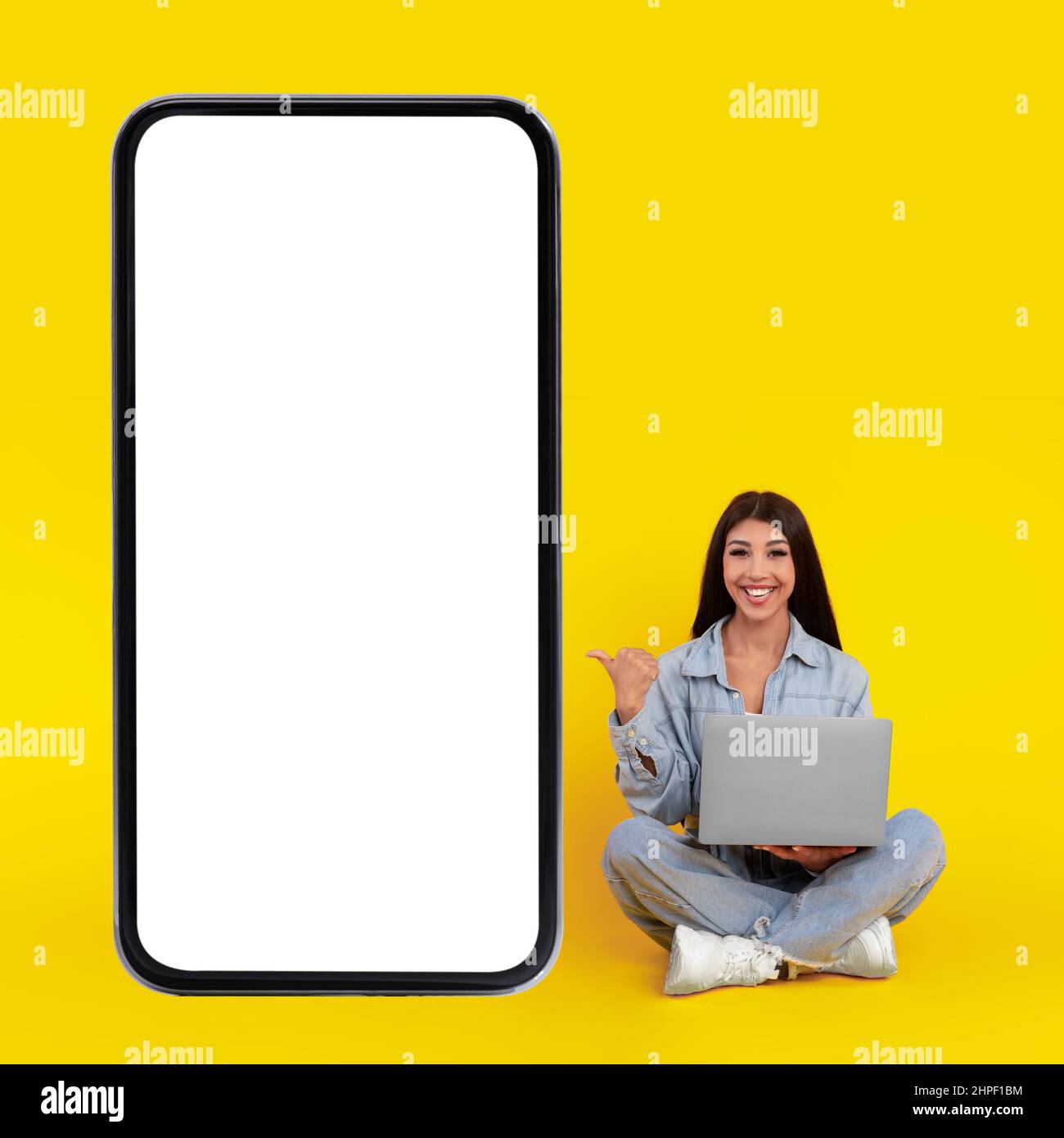 Signora felice usando il pc che punta al grande schermo del telefono cellulare Foto Stock