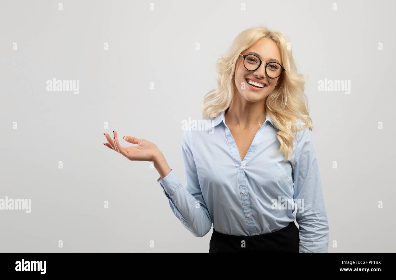 Offerta business. Felice donna d'affari bionda che dimostra qualcosa al suo palmo vuoto e sorride alla macchina fotografica Foto Stock