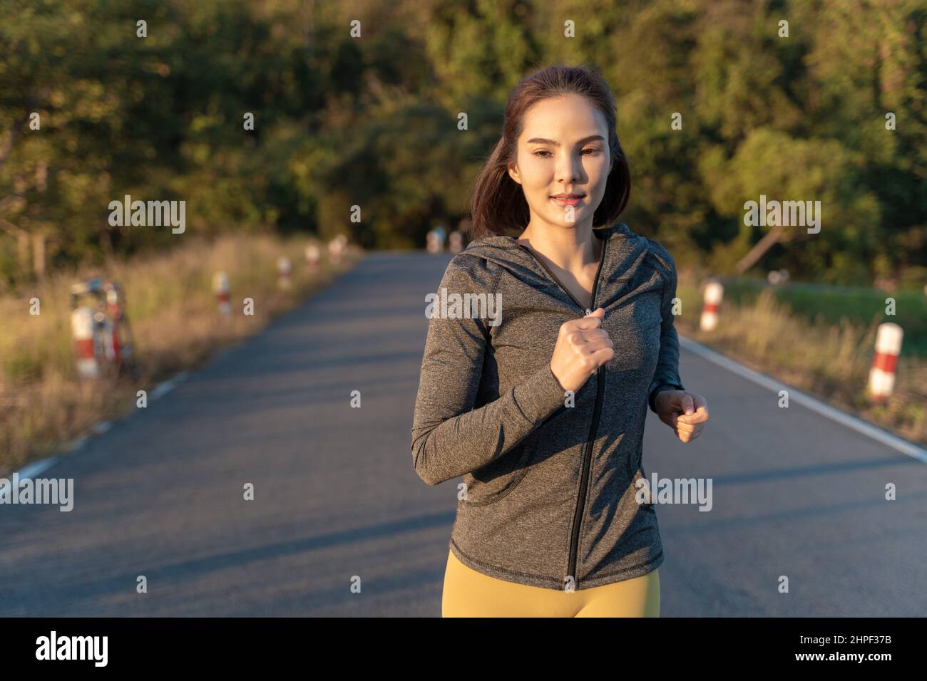 Felice attraente giovane donna che indossa il suo giubbotto riscaldato mentre corre in un parco locale durante la sua routine di esercizio mattutino Foto Stock