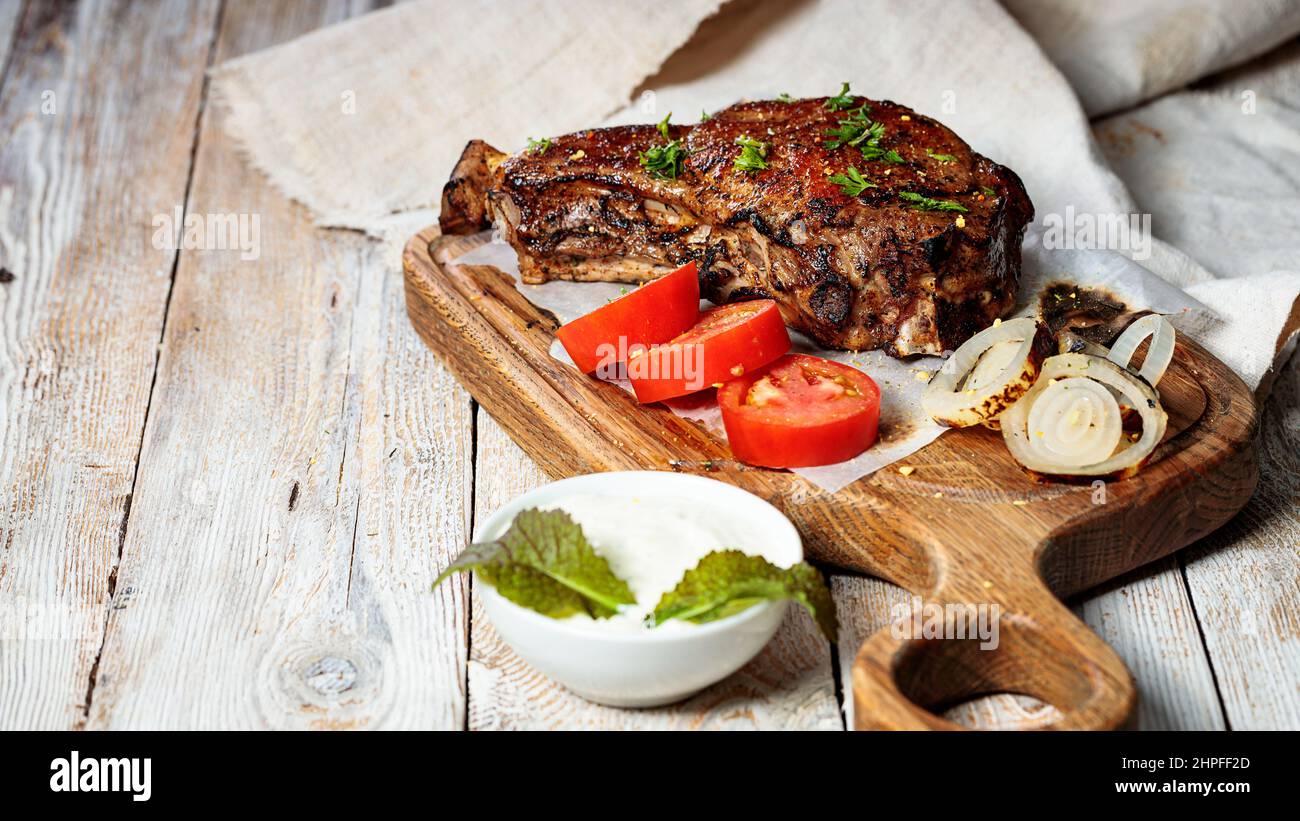 Bistecca alla griglia su un tagliere. Carne arrosto appetitosa con verdure ed erbe. Spazio di copia. Rustico sfondo tavolo in legno. Foto Stock