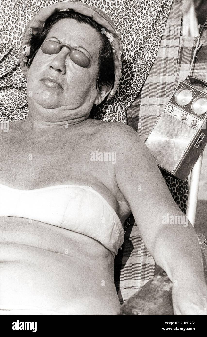 Una donna che si prende il sole a Brighton Beach ascoltando una radio a transistor e indossando protezioni in plastica per gli occhi. A Brooklyn, New York, circa 1976. Foto Stock