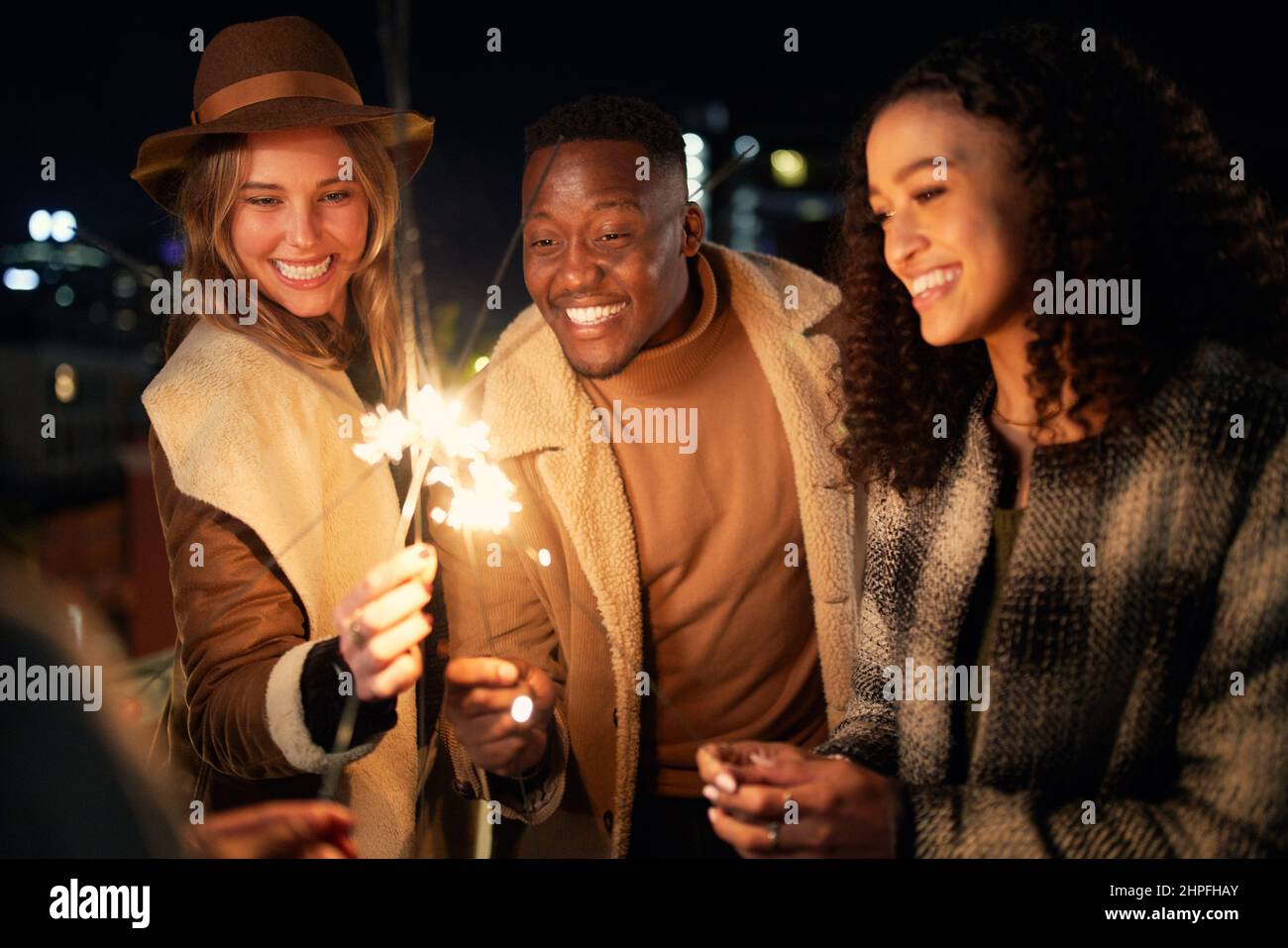 Gruppo di amici alla moda multiculturale che sorridono a una festa di luci scintillanti. Vita notturna in città Foto Stock