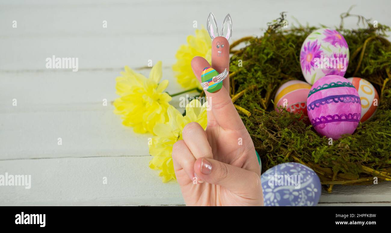 Mano tagliata con cartone animato creativo che si disegna sulle dita incrociate sopra le uova di pasqua nel nido Foto Stock