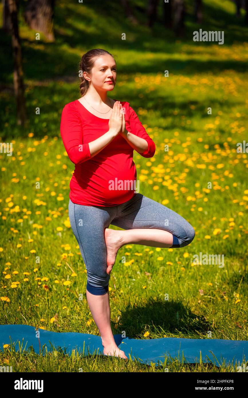 Donna incinta che fa asana vrikshasana all'aperto Foto Stock