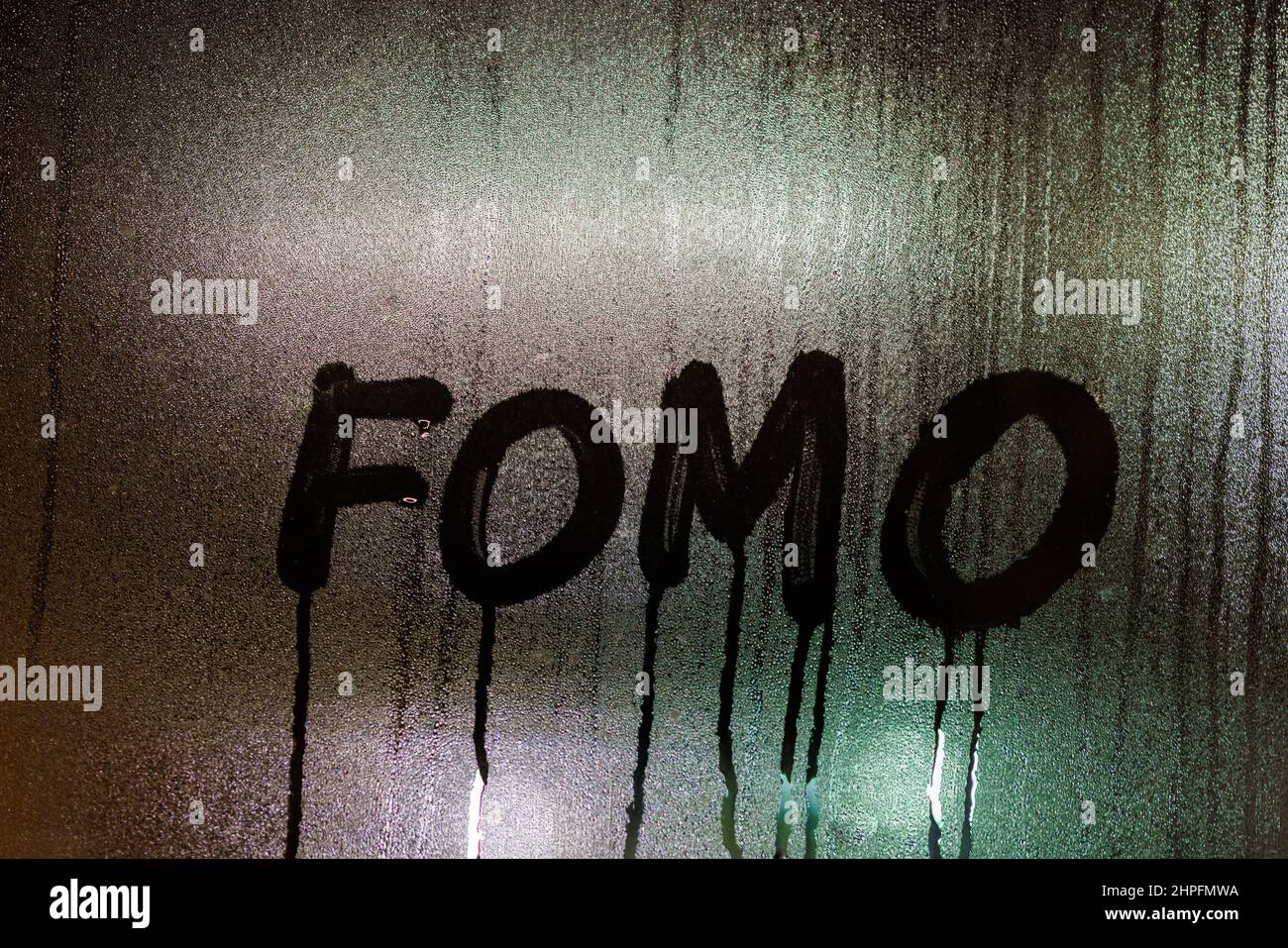 Parola FOMO - paura di scomparire - scritto a mano sulla superficie bagnata del vetro della finestra di notte Foto Stock