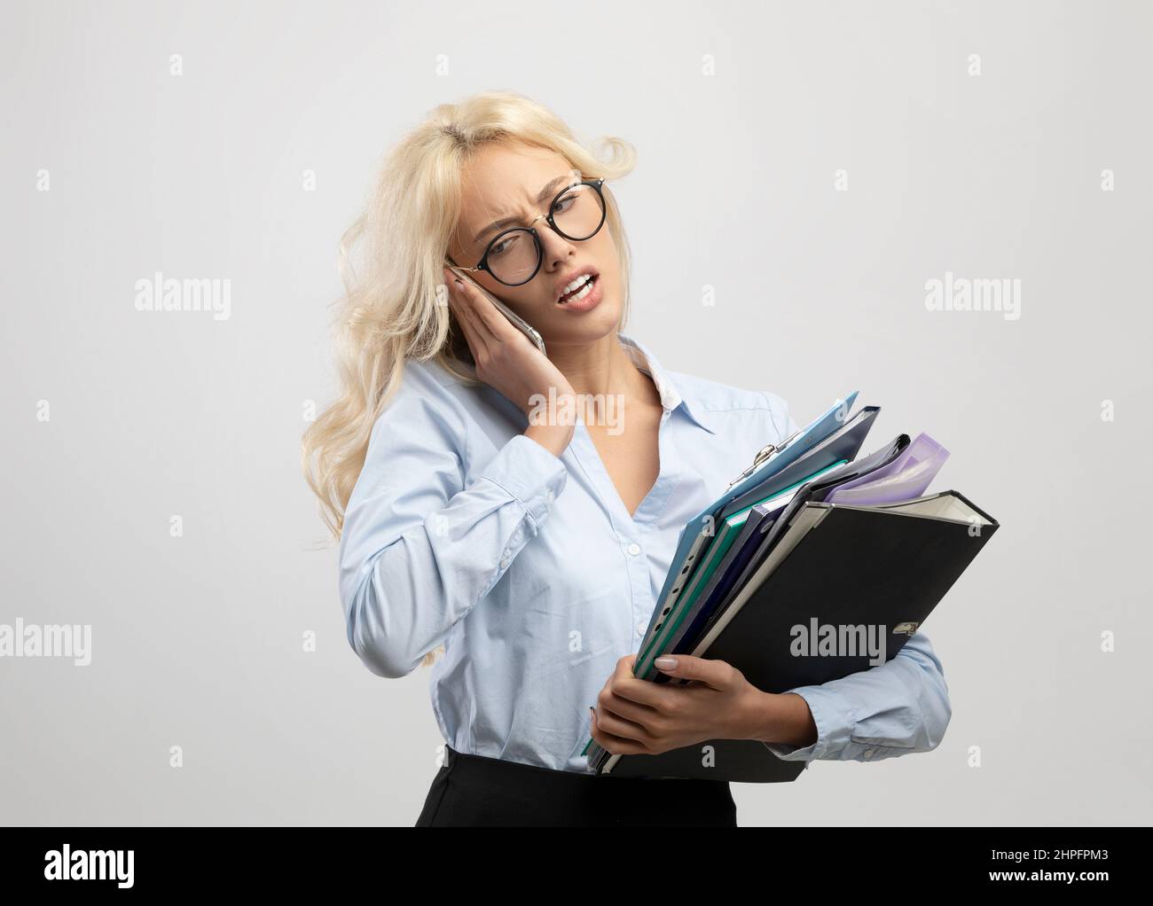 Vecchio lavoratore di ufficio con un mucchio di cartelle che parlano sul cellulare, avendo un sacco di lavoro, in piedi su sfondo chiaro Foto Stock