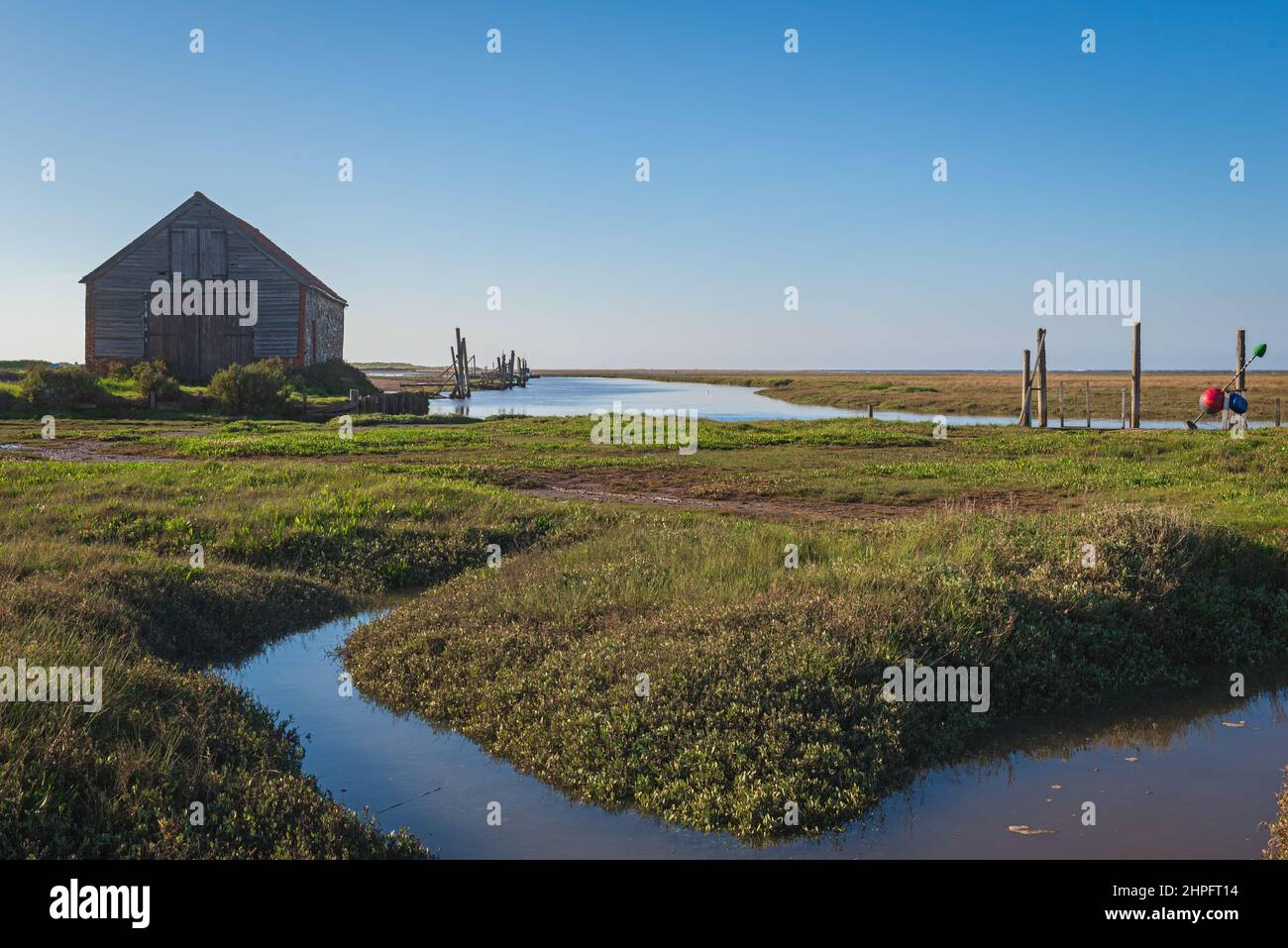 Il Coal Barn a Thornham Old Harbour è circondato da acque alluvionali mentre la marea entra in una soleggiata serata primaverile. Thornham, Norfolk, Inghilterra, Regno Unito Foto Stock