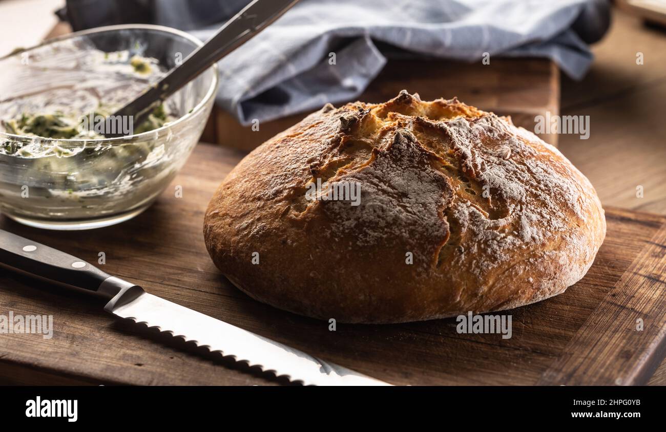 Pane croccante accanto a un coltello e burro mescolato con erbe in una ciotola. Foto Stock