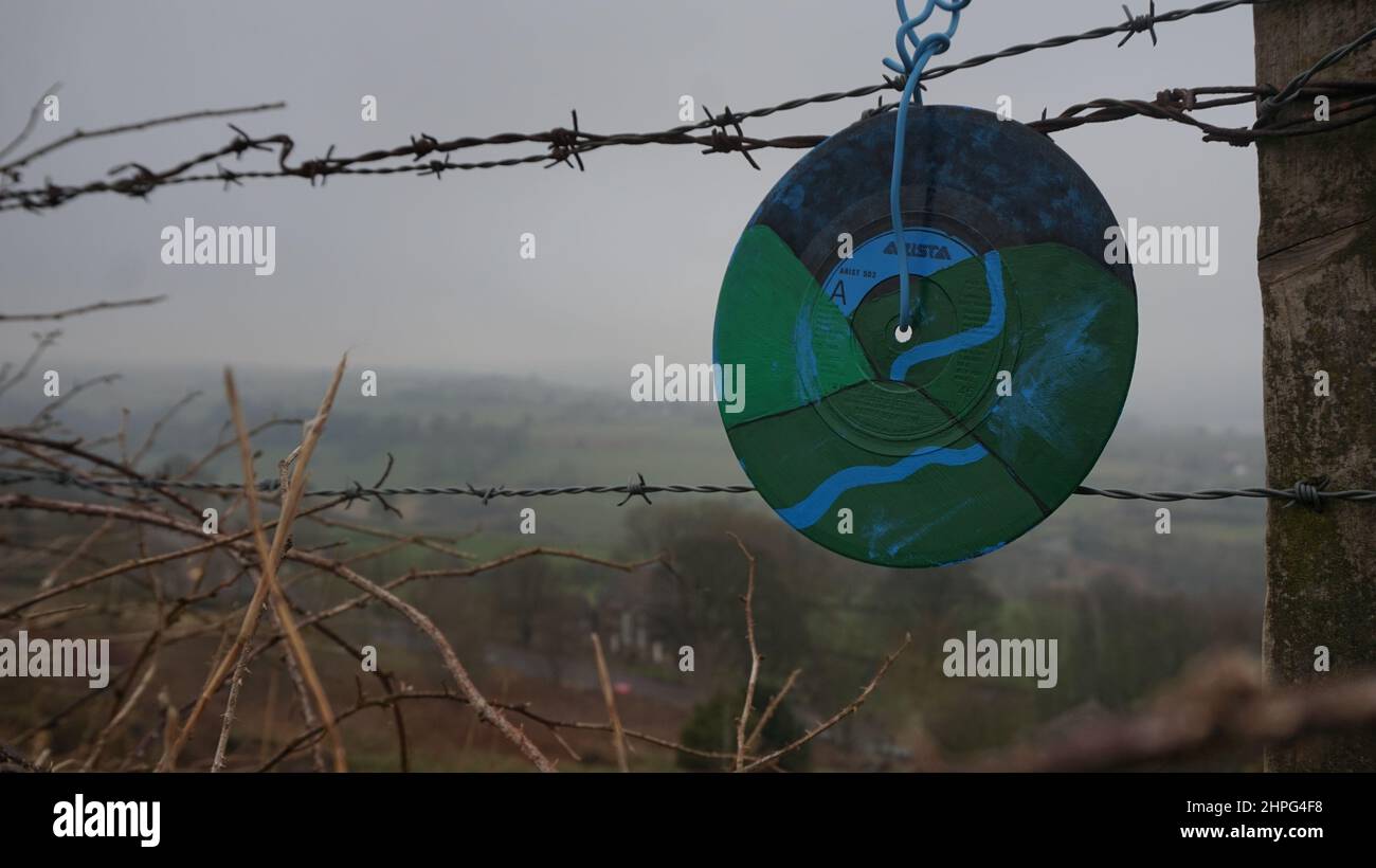 Singoli in vinile, dipinti con disegni astratti, esposti sulla scherma in campagna. Arte di strada Anonimo. Derbyshire. Foto Stock