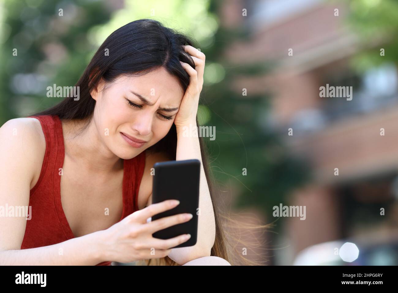 Donna asiatica preoccupata che controlla lo smartphone per strada Foto Stock