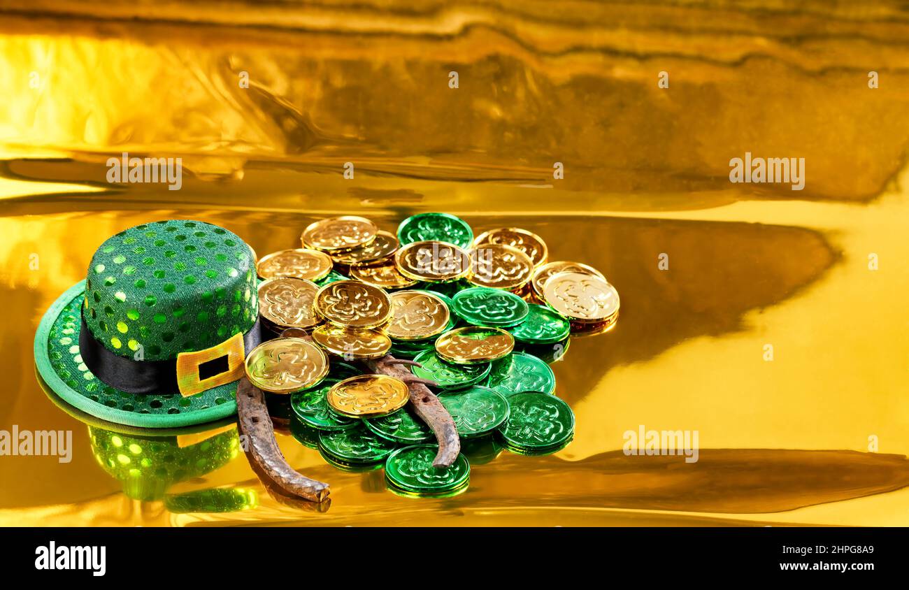Cappello verde di buona fortuna, ferro di cavallo e monete per il giorno di San Patrizio su sfondo dorato Foto Stock