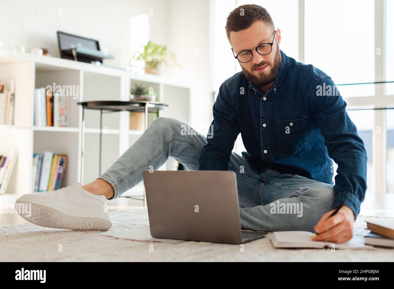 Uomo che prende appunti utilizzando il portatile seduto sul pavimento a casa Foto Stock