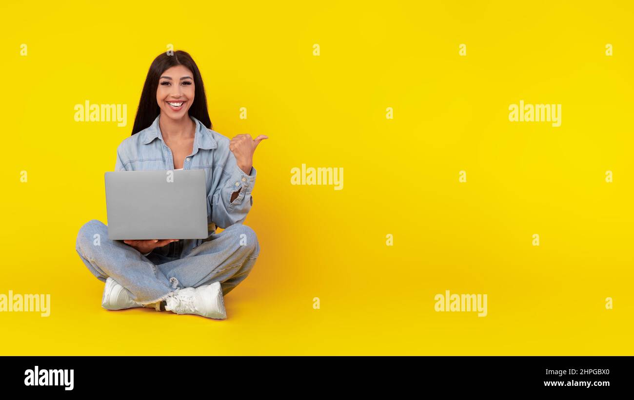 Signora felice usando il laptop che punta da parte allo studio Foto Stock