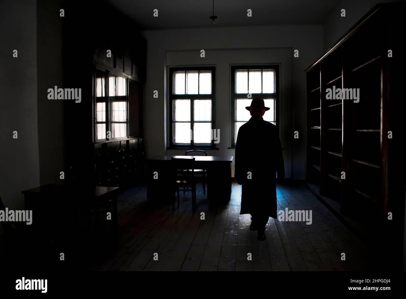 uomo misterioso in cappotto lungo e cappello fedora, camminando all'interno di una stanza buia Foto Stock