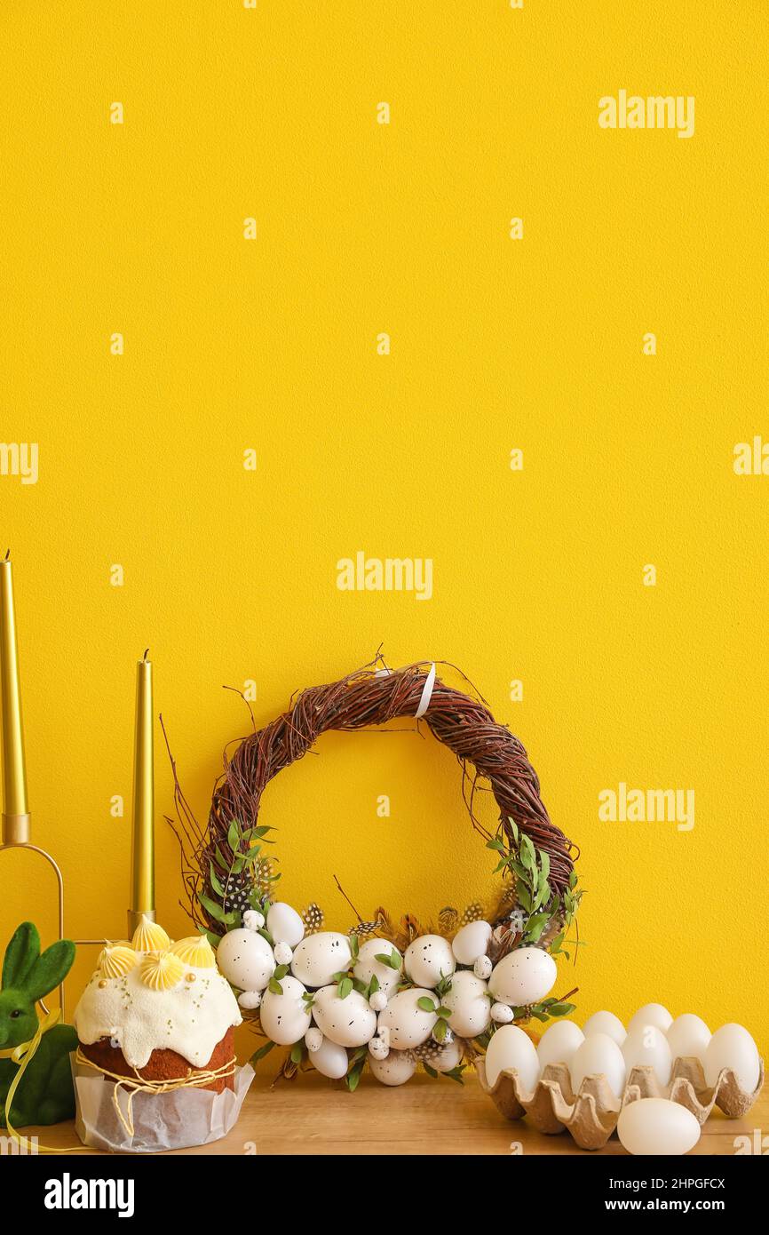 Bella corona di Pasqua fatta a mano, torta e uova sul tavolo vicino muro di colore Foto Stock