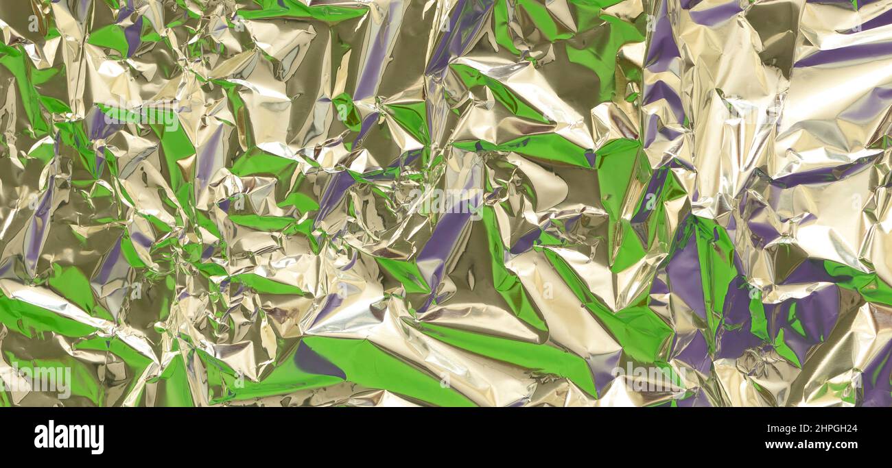 Astratto argento alluminio rugoso foglio multicolore sfondo tessuto riflettente verde e viola luce. Lucentezza metallizzata in lamina argentata Foto Stock