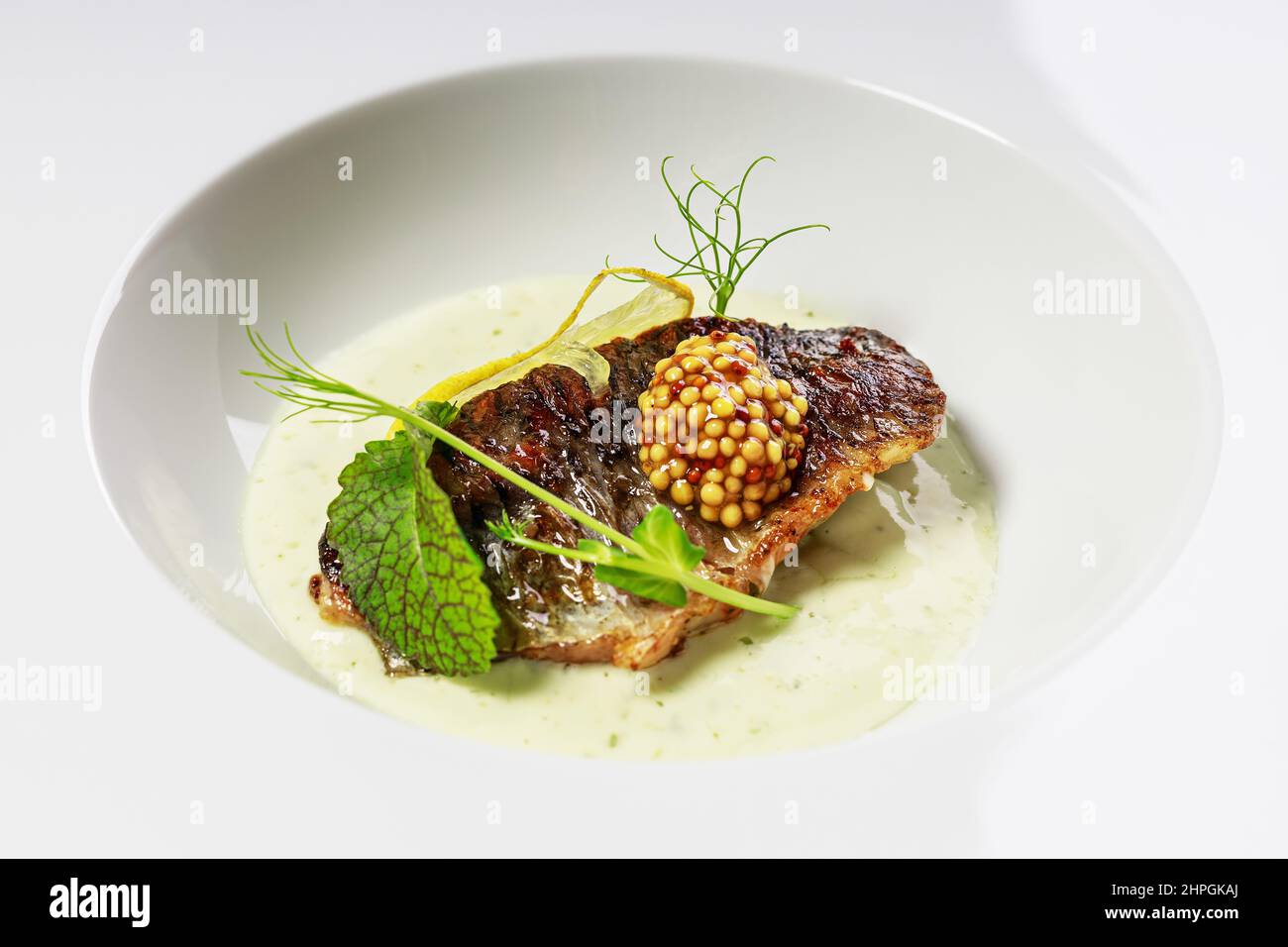 Filetto di pesce alla griglia con salsa, senape ed erbe su un piatto bianco. Primo piano. Il ristorante serve. Frutti di mare foto Foto Stock