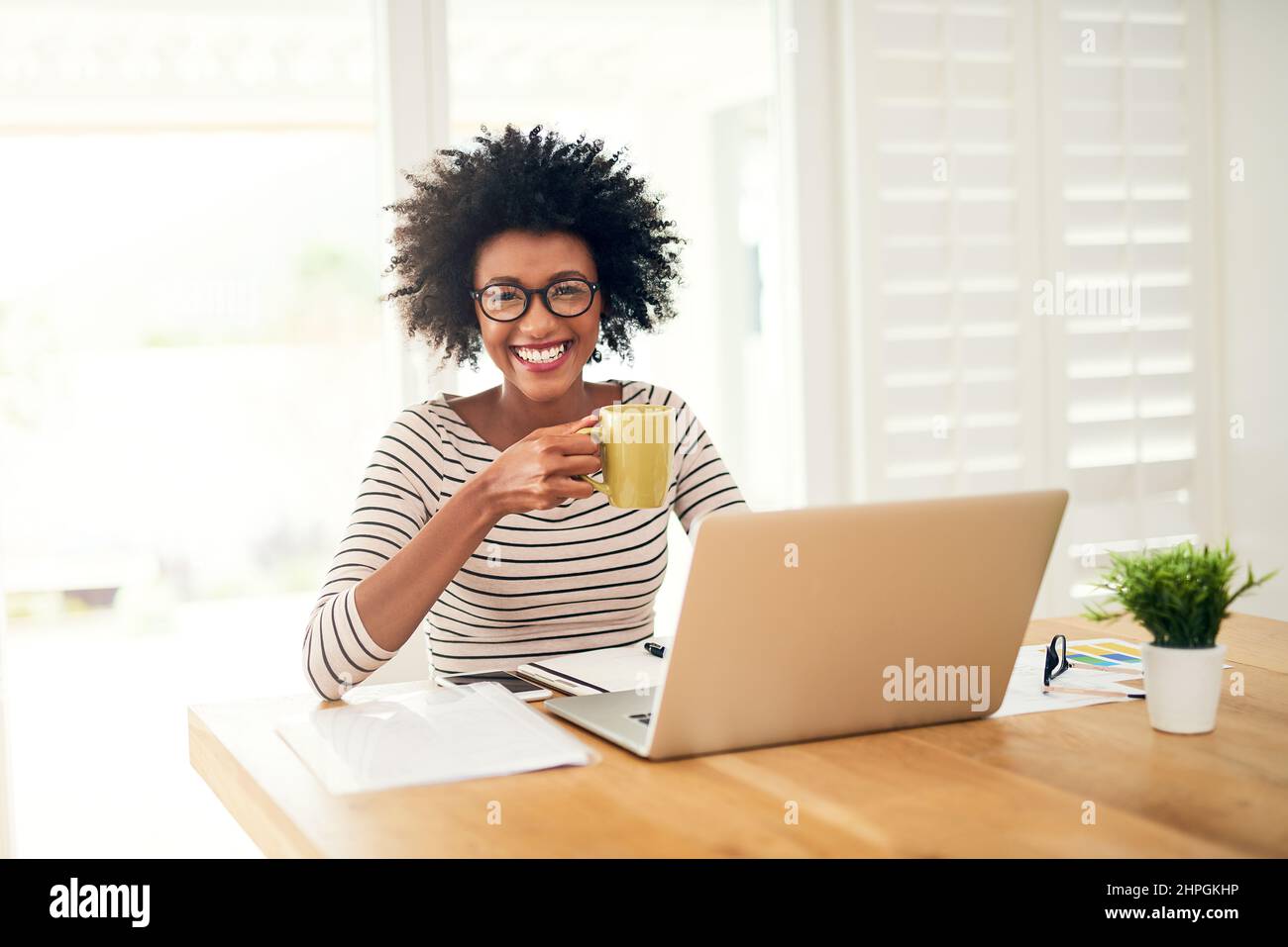 Niente di meglio di una tazza di comfort per iniziare la giornata. Ritratto di una giovane donna che beve caffè mentre lavora sul suo portatile a casa. Foto Stock