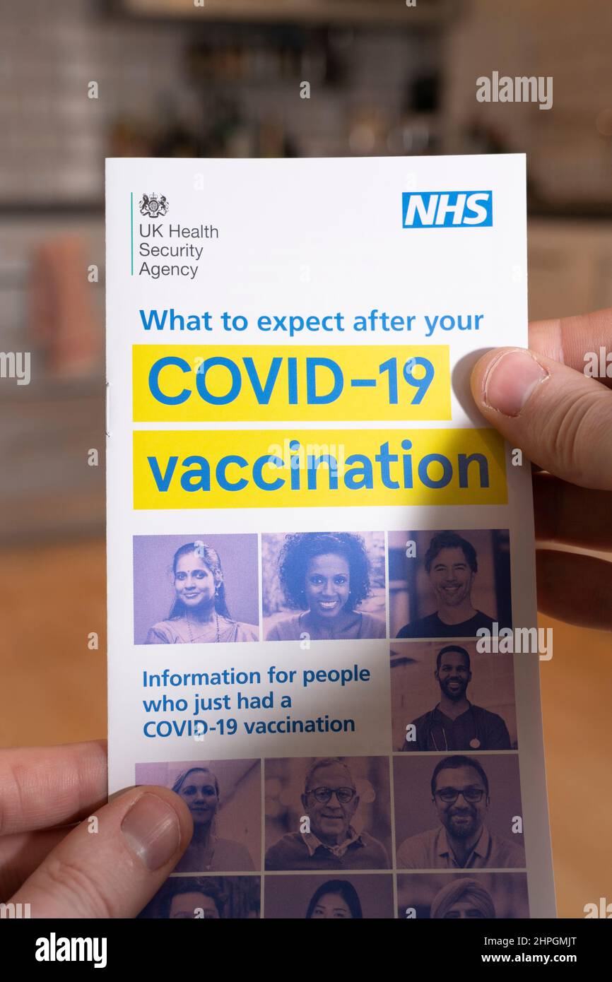 Le mani di un uomo che tiene un'agenzia di sicurezza del governo del Regno Unito e un opuscolo NHS che fornisce consigli su cosa accade dopo una vaccinazione di Coronavirus Covid-19 Foto Stock