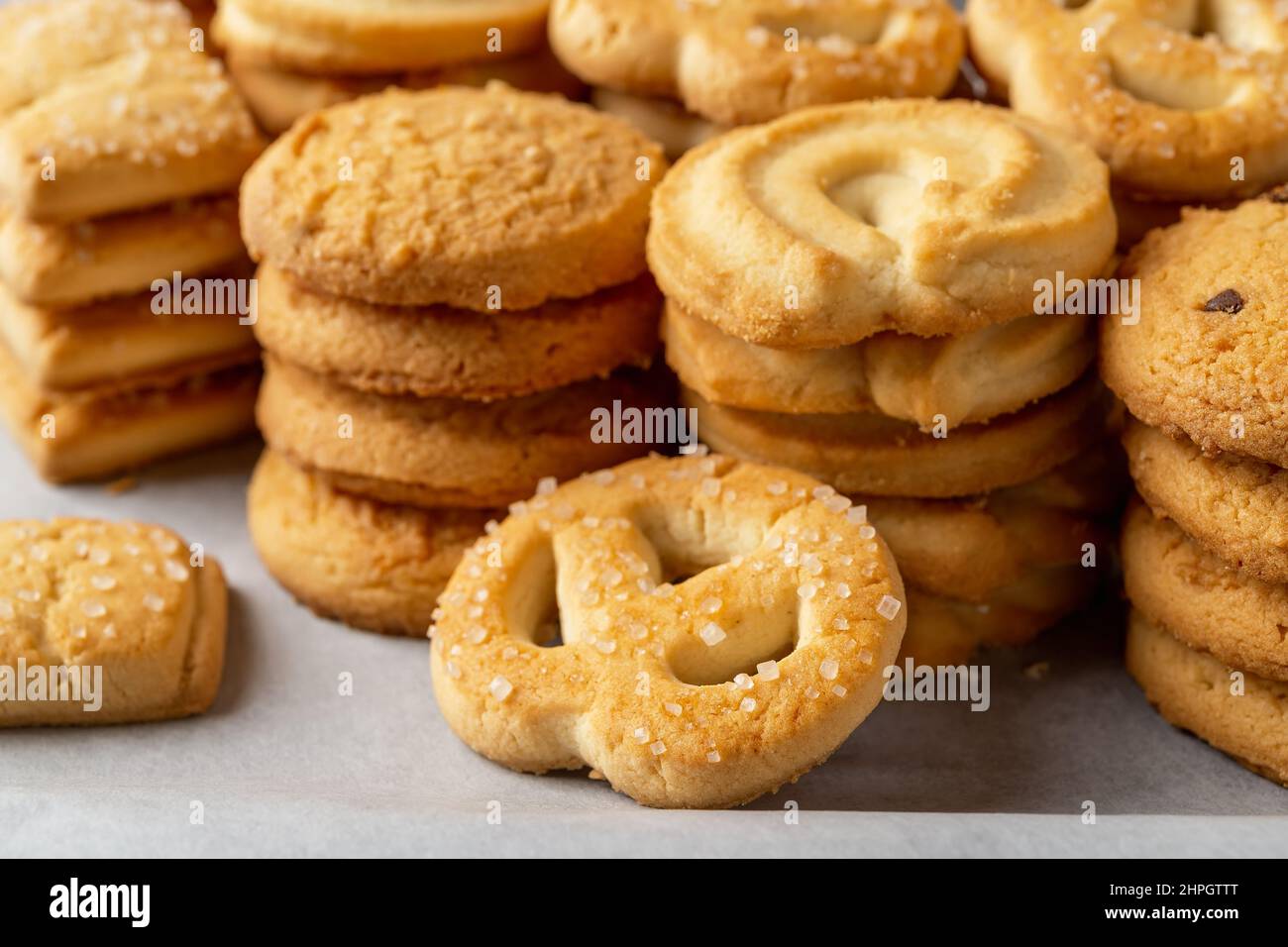 Zucchero pretzel contro di biscotti accatastati di shortbread su una pergamena da forno bianca. Primo piano con biscotti al burro croccanti assortiti. Gustosa pasticceria danis. Macro. Foto Stock