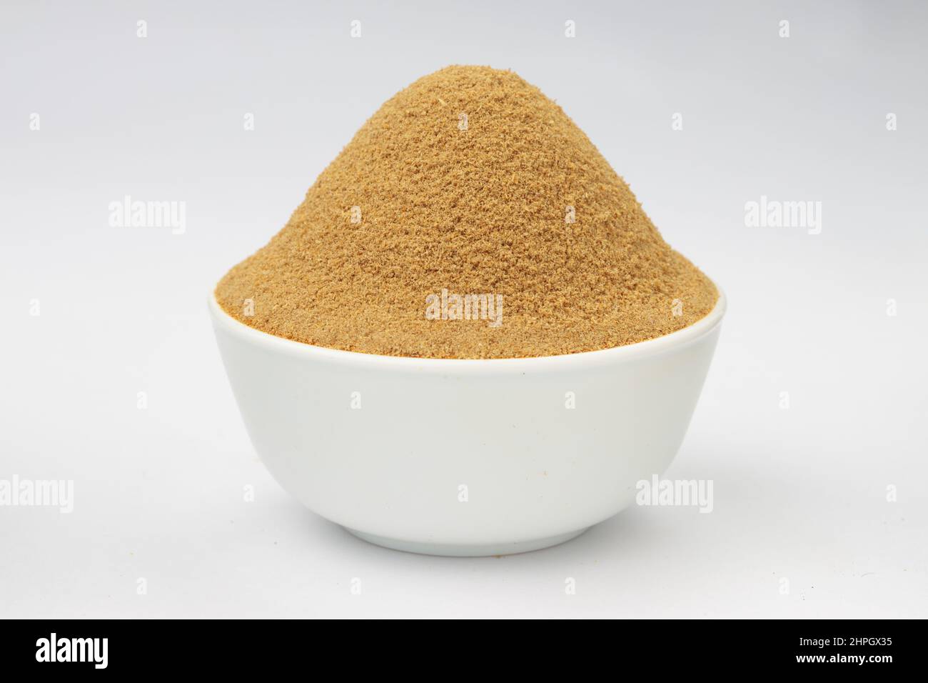 Polvere di coriandolo ,spezia indiana ; ingrediente principale per i piatti indiani , disposto in una ciotola bianca su uno sfondo bianco testurizzato. Foto Stock