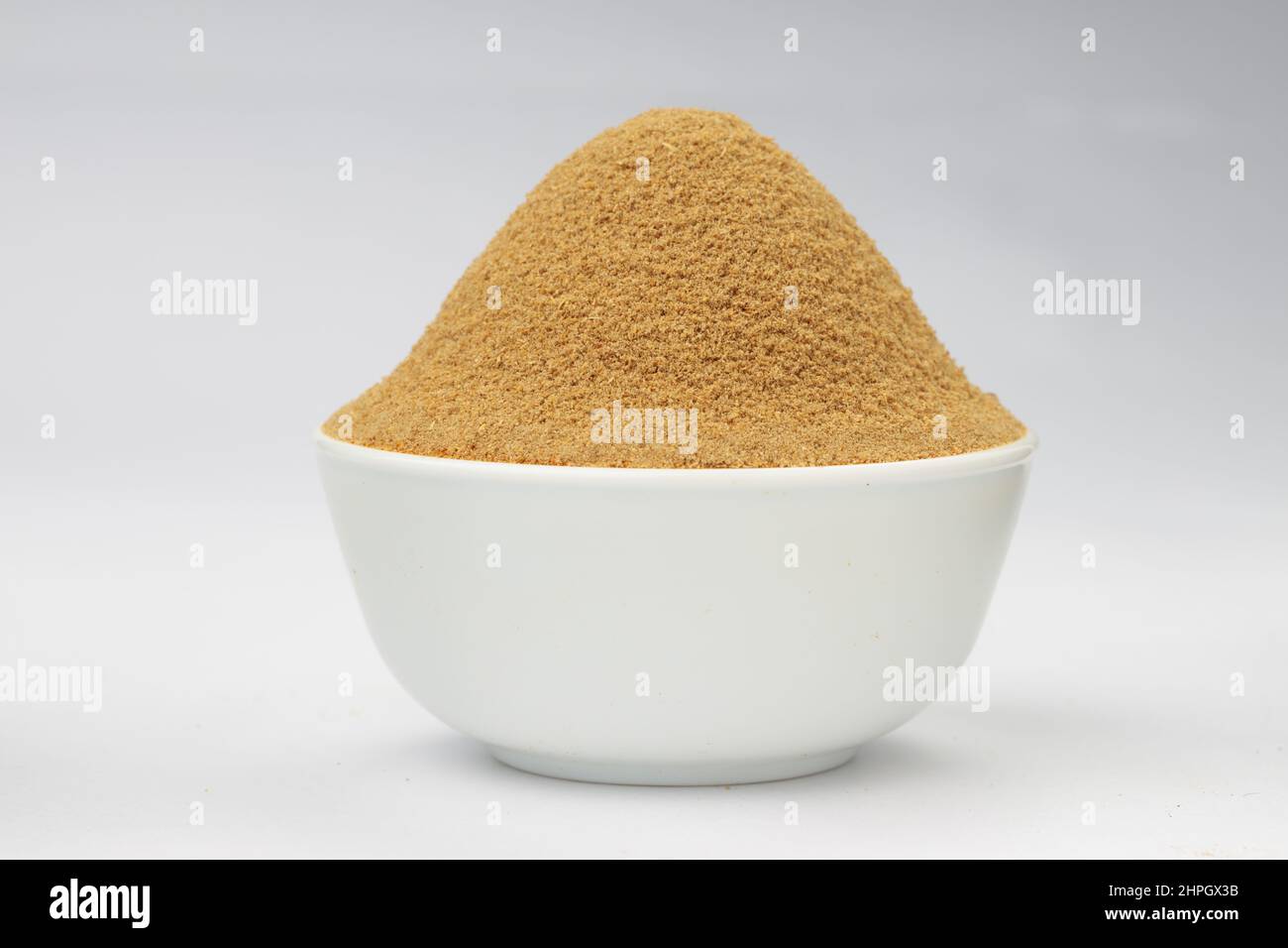 Polvere di coriandolo ,spezia indiana ; ingrediente principale per i piatti indiani , disposto in una ciotola bianca su uno sfondo bianco testurizzato. Foto Stock