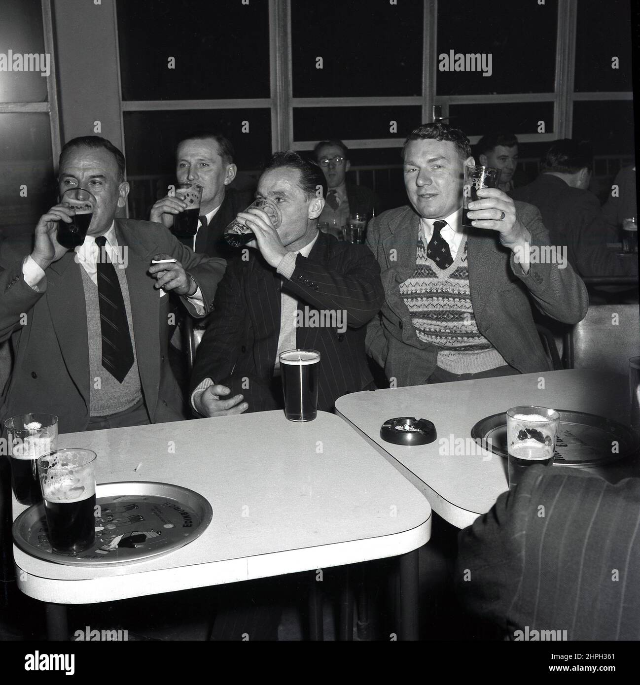 1950s, storico, all'interno del club sociale, seduto ad un piccolo tavolo, un gruppo di lavoratori siderurgici che godono di una pinta di birra dopo il loro turno, Port Talbot, Galles, Regno Unito. Foto Stock