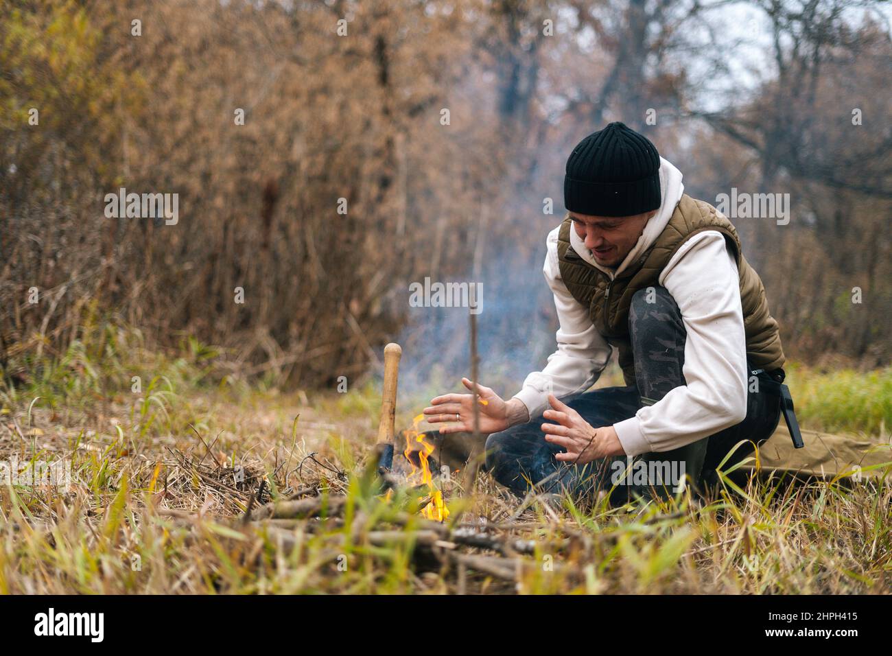 Ritratto di surgelato uomo turistico indossare abiti caldi scaldando le mani sul fuoco all'aperto in giornata fredda coperto. Foto Stock