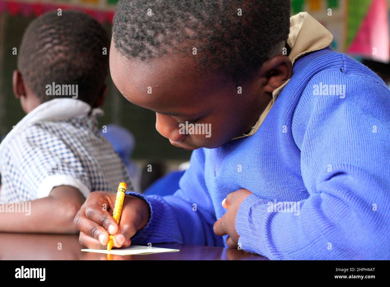 Un giovane ragazzo scrive con un pastore presso la Macheke Primary School. I giovani allievi usano i pastelli mentre imparano scrivere. Zimbabwe. Foto Stock