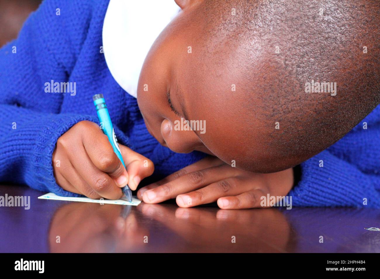 Una giovane ragazza scrive con un pastore alla Scuola primaria di Macheke. I giovani allievi usano i pastelli mentre imparano scrivere. Zimbabwe. Foto Stock