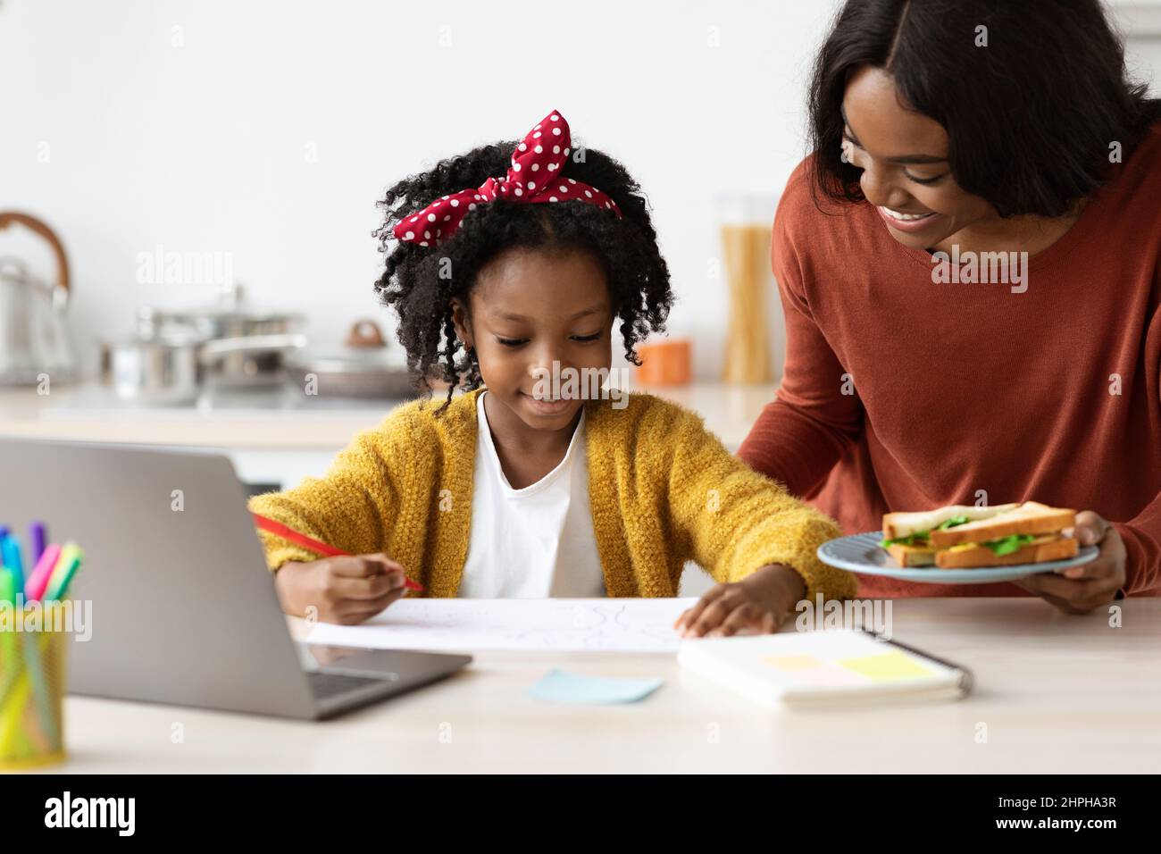 La mamma nera che si prende cura porta spuntini a studio con il portatile a casa Foto Stock
