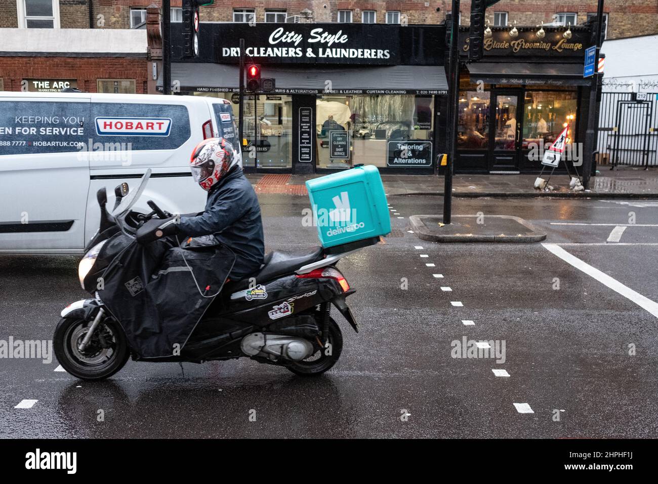 Deliveroo delivery rider fa la sua strada lungo una Londra affollata in una giornata di inverni bagnati. Foto Stock