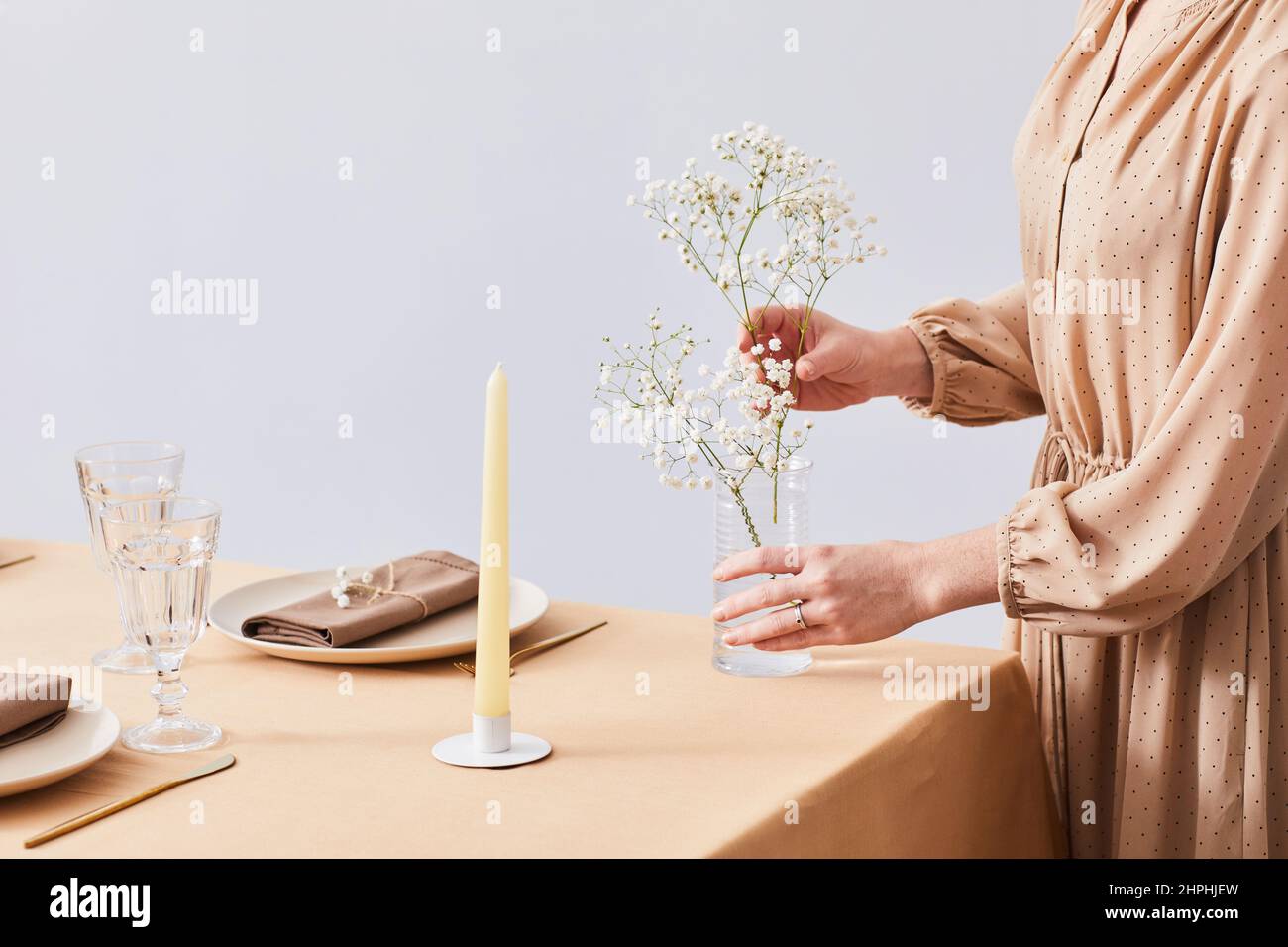 Primo piano minimo di giovane donna decorazione tavolo da pranzo con eleganti fiori dainty per la primavera, spazio copia Foto Stock
