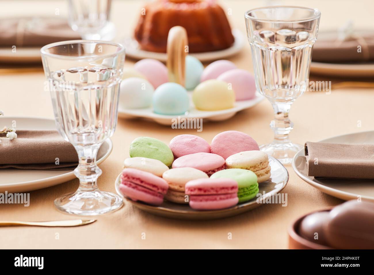 Primo piano di deliziosi piatti di macaroon su un elegante tavolo da pranzo decorato per Pasqua e primavera, spazio copia Foto Stock