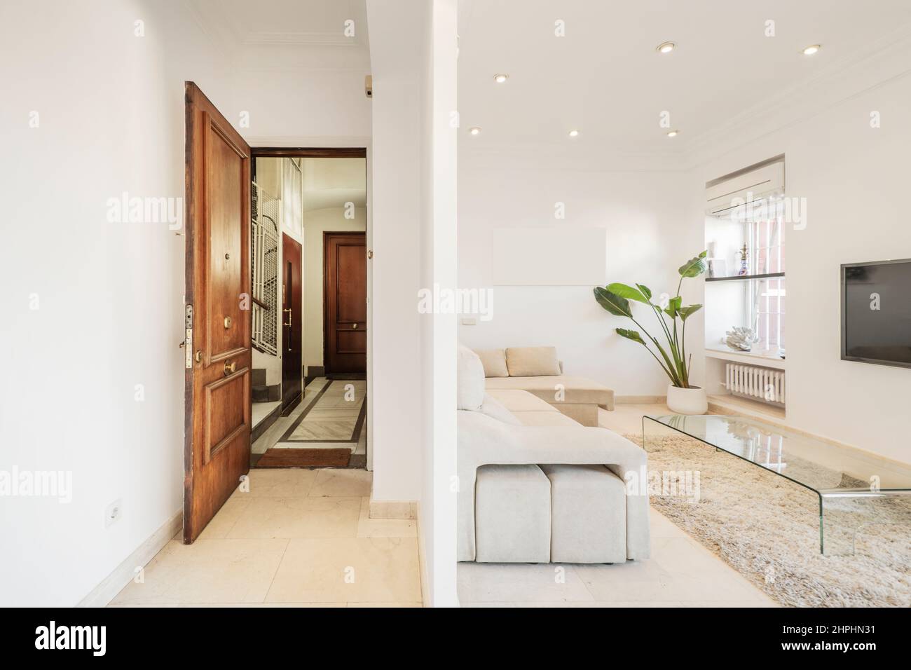 Ingresso ad una casa con una sottile parete che separa la sala da un soggiorno con TV e tavolo in metacrilato Foto Stock