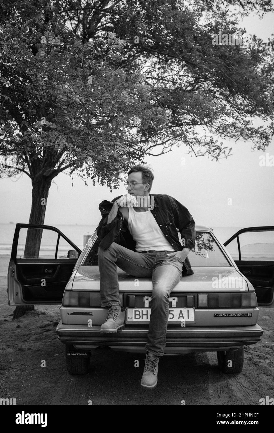 bell'uomo in occhiali vicino auto e albero bianco e nero Foto Stock