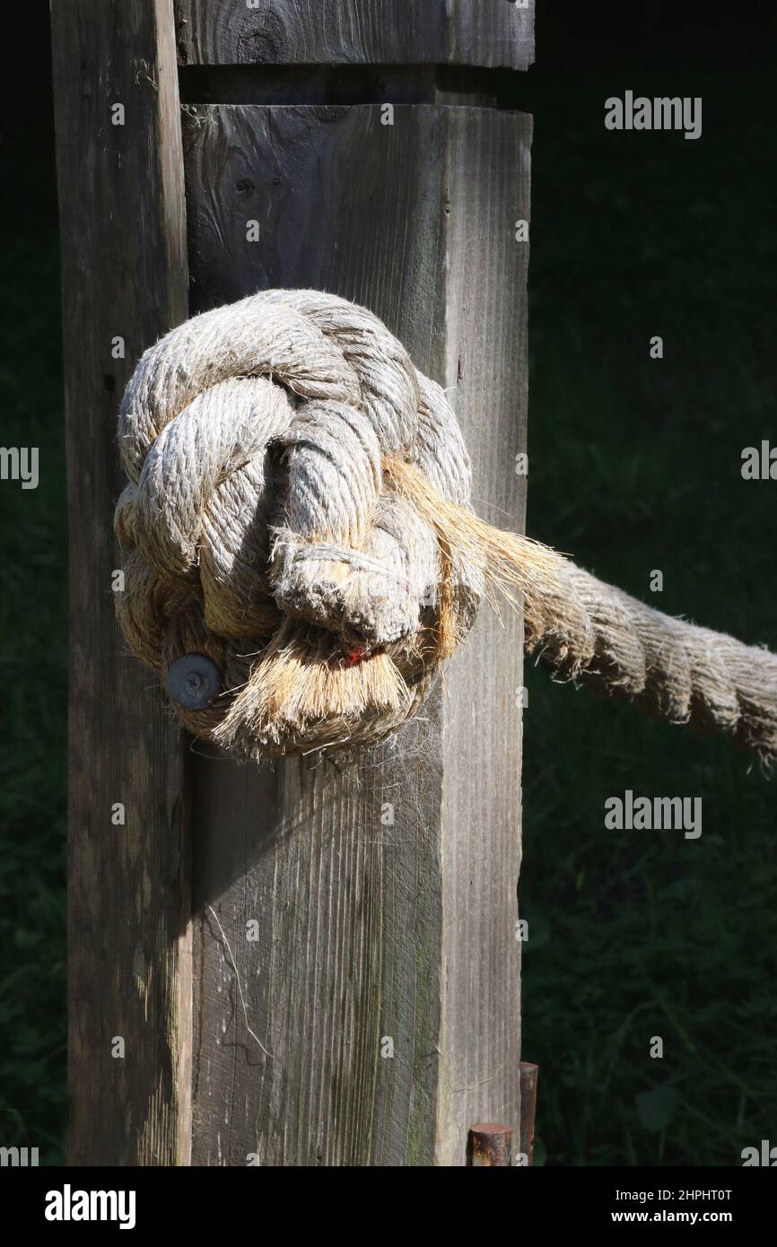 Corda sfilacciata legata in un nodo su un palo di legno intemperiato. Foto Stock