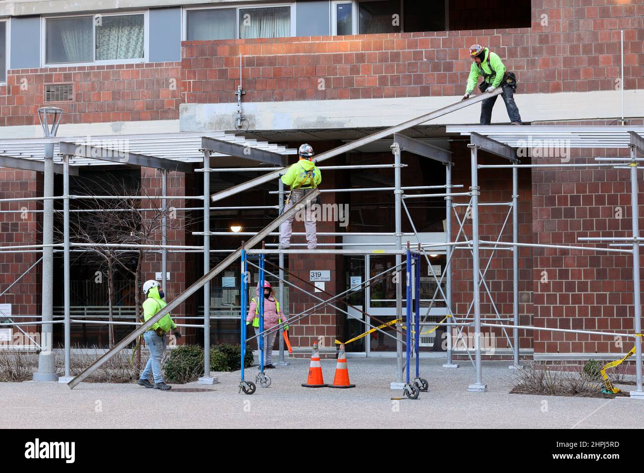I lavoratori di un'azienda di sollevamento del capannone del marciapiede sollevano le travi metalliche sulla parte superiore del ponteggio del marciapiede in costruzione a New York City Foto Stock