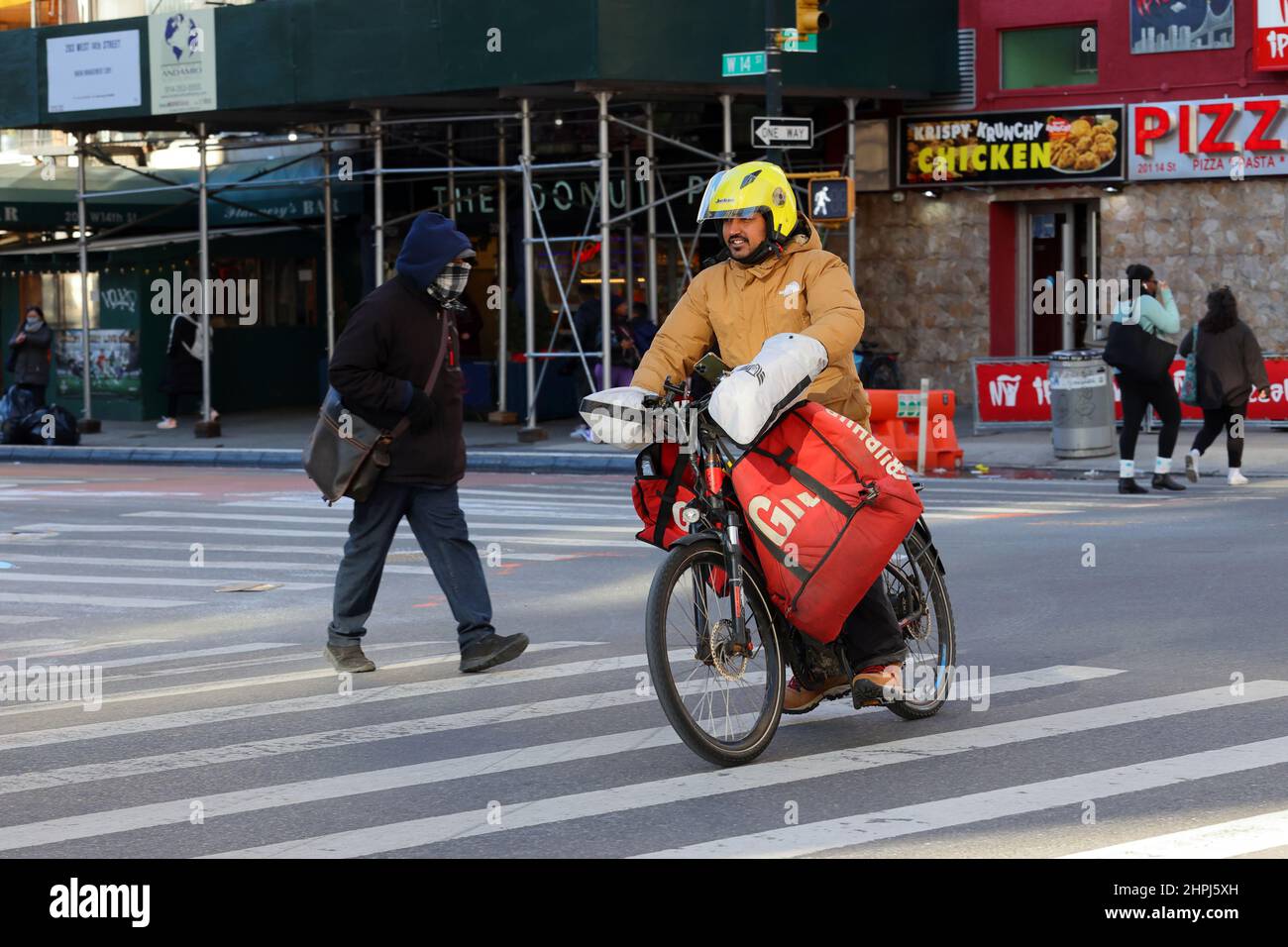 Una persona con consegna di cibo a Grubbub su una bicicletta elettrica passa davanti a un incrocio a New York City Foto Stock