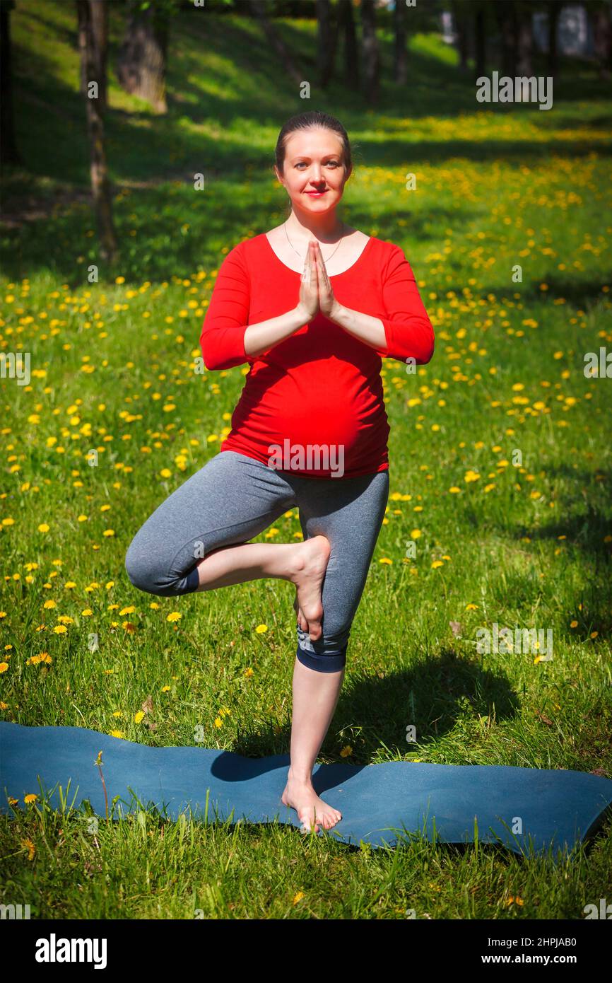 Donna incinta che fa asana vrikshasana all'aperto Foto Stock