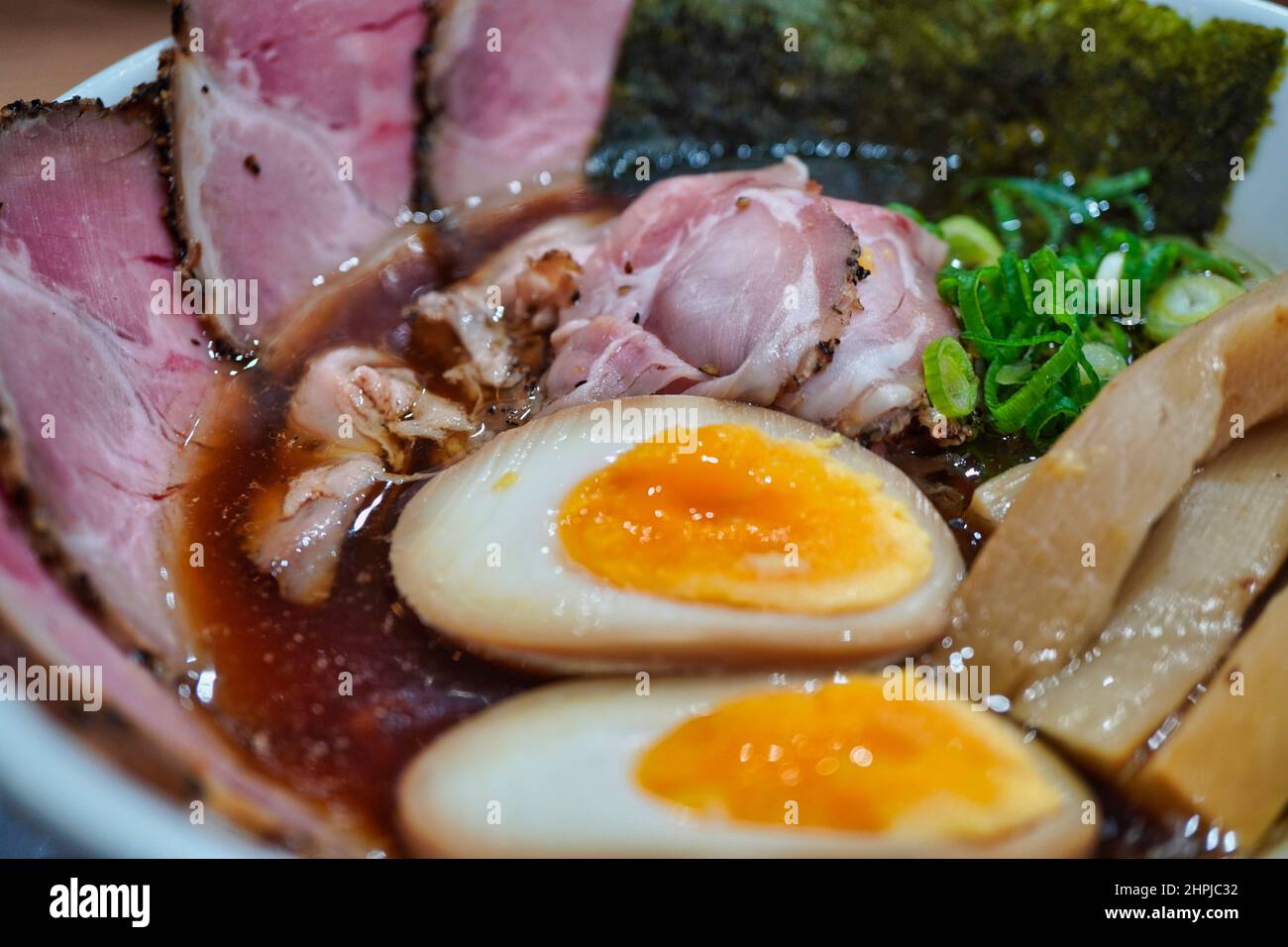 un primo piano di una ciotola di zuppa con salamoia marinata, uovo sodo, maiale affettato e carne, nori, grasso e bontà da cipolla verde fresca e tritata. Foto Stock
