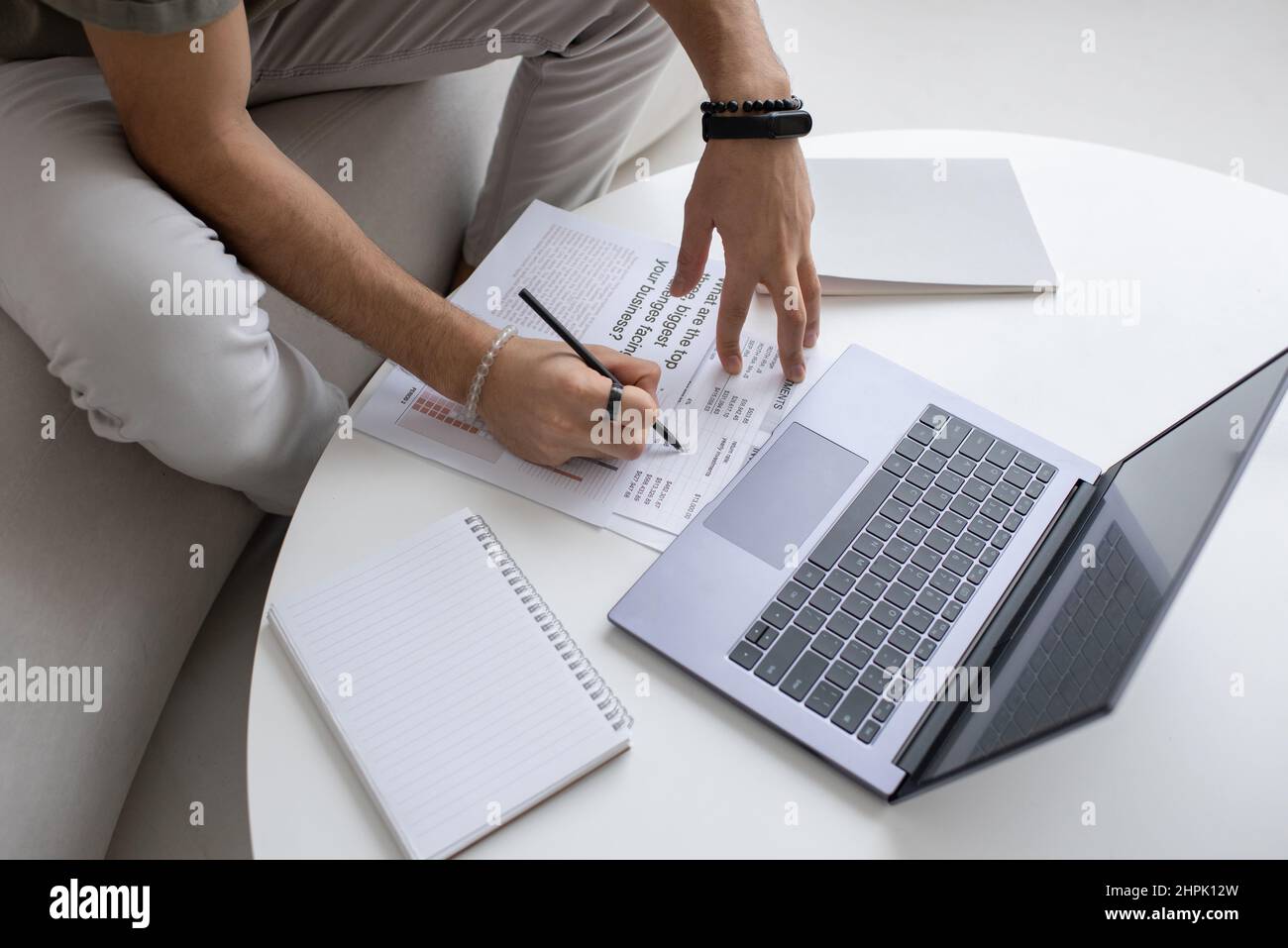Le mani di un giovane economista o analista con una penna che punta verso un documento finanziario mentre analizzano i dati davanti al laptop per tabella Foto Stock