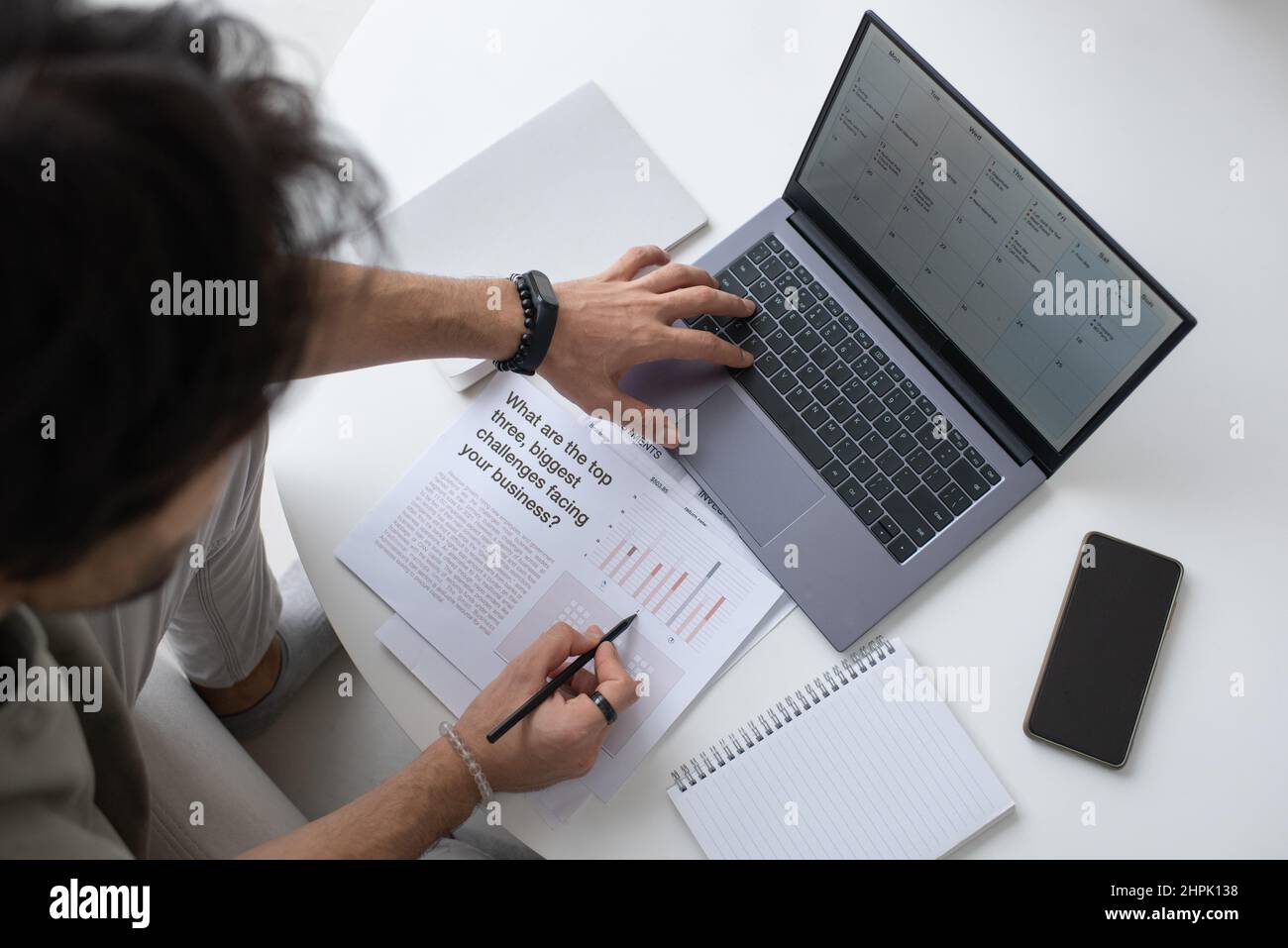 Auditor o analista contemporaneo che esamina il testo nel documento e analizza i dati finanziari sullo schermo del notebook mentre lavora da casa Foto Stock