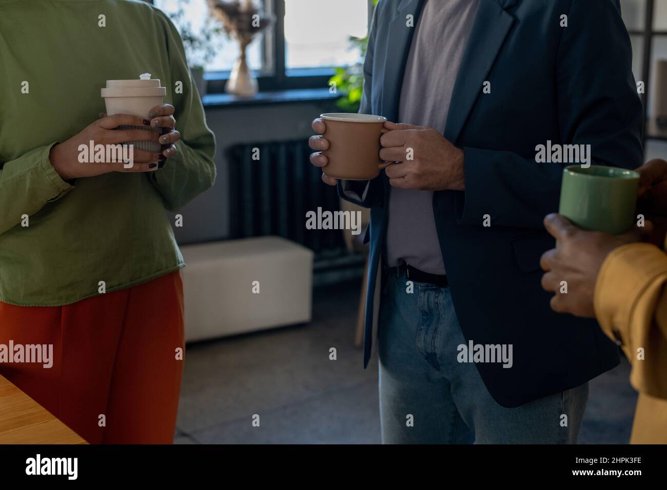 Gruppo di eleganti impiegati maschili e femminili in astuti casualwear che bevono e parlano a pausa mentre si levano in piedi l'uno di fronte all'altro Foto Stock
