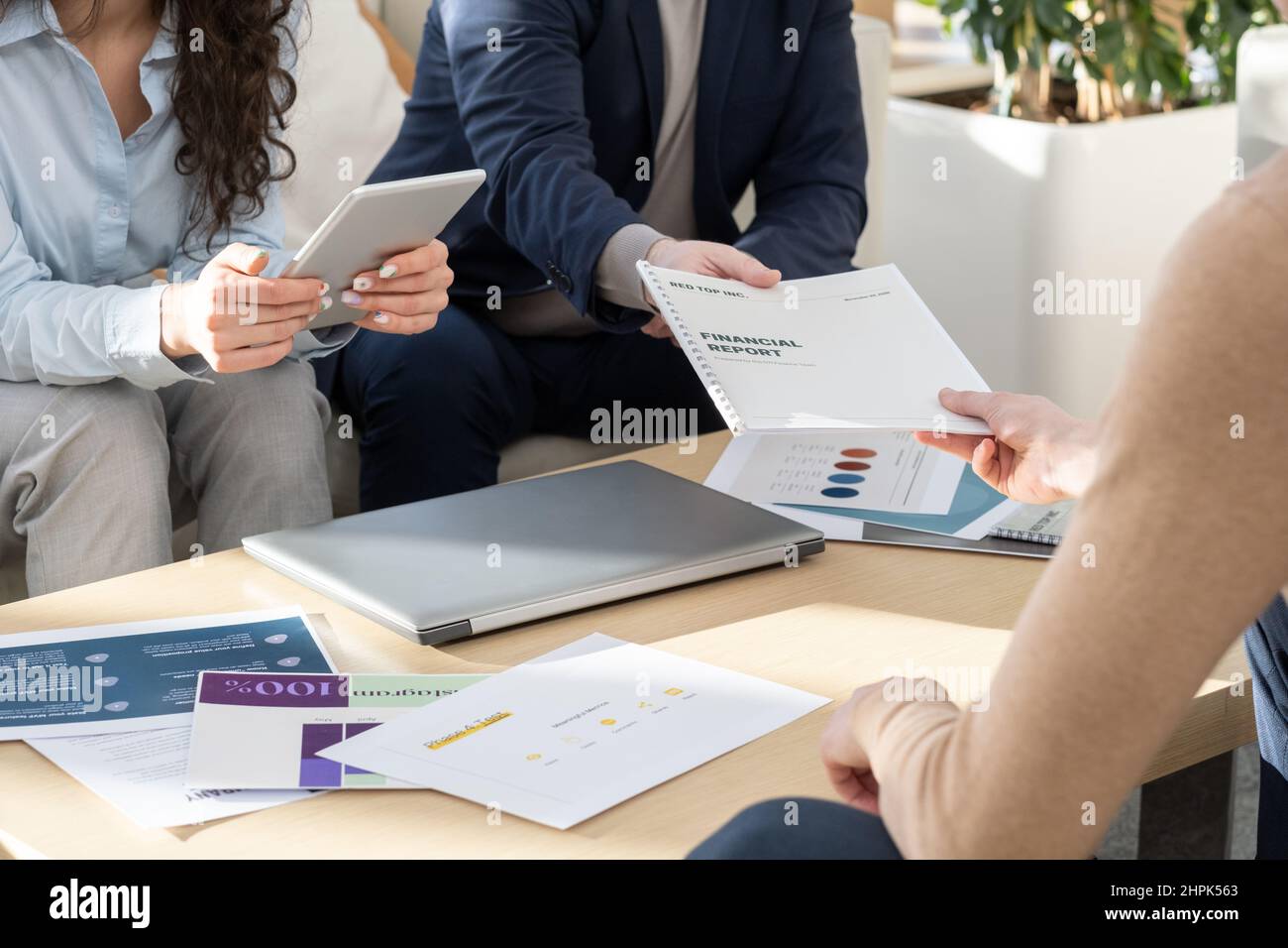 Un uomo d'affari in grado di trasmettere il rapporto finanziario a uno dei colleghi al tavolo con documenti e laptop durante la riunione di lavoro in ufficio Foto Stock