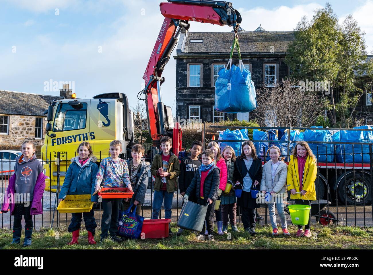 Trinity Primary School, Edimburgo, Scozia, Regno Unito, 22 febbraio 2022. Topsoil Botanico per le scuole: Scavo durante il Royal Botanic Garden Biomes Project risulta in un'eccedenza di 50 tonnellate di topsoil che è dato alle scuole, allotments & organizzazioni della comunità dalla società di costruzione Balfour Beatty. Una consegna di 5 tonnellate avviene presso la Trinity Primary School per trasportare il suolo o la terra per riempire piantatrici nel giardino della scuola per gli allievi per coltivare le verdure. Gli allievi primari 4 usano contenitori di tutte le forme e dimensioni per spostare la terra per riempire le piantatrici; lavoro di squadra è richiesto Foto Stock